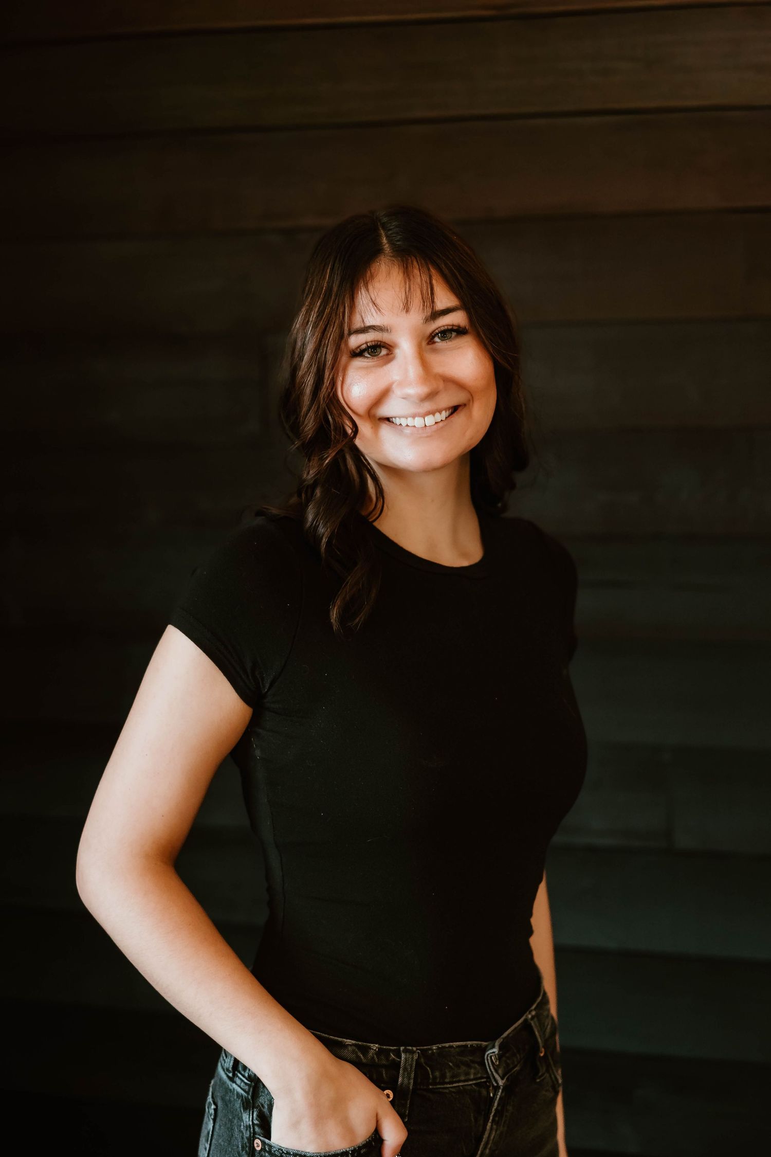 Professional wearing black attire poses against dark wooden wall with confident expressions.