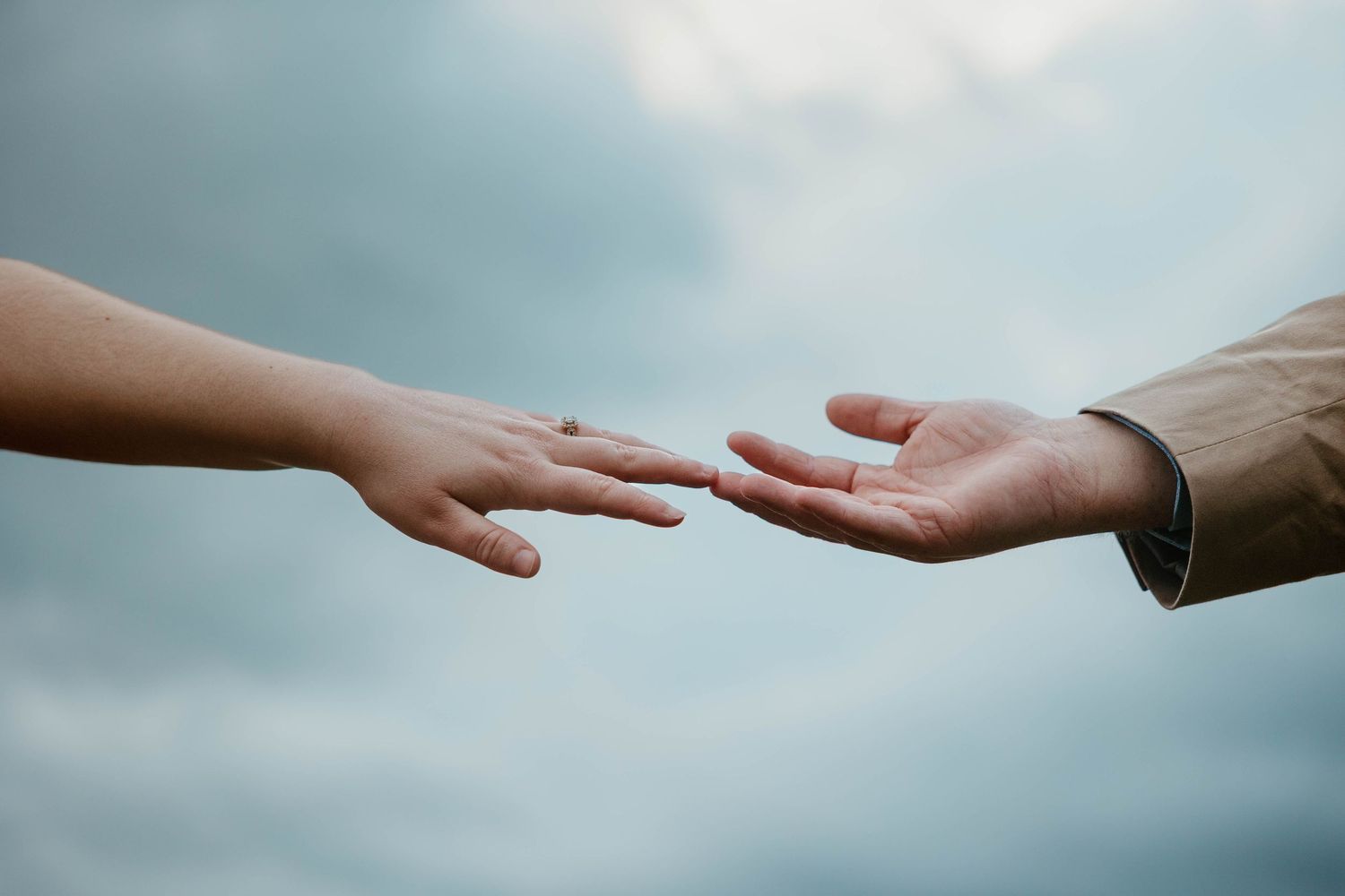 Hands reaching towards each other against a soft blue sky background.