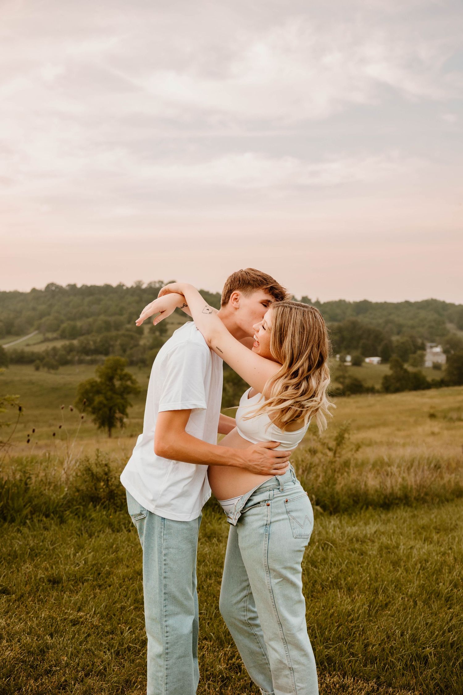 A romantic couple dances and embraces in a sunlit field with rolling hills in the background.