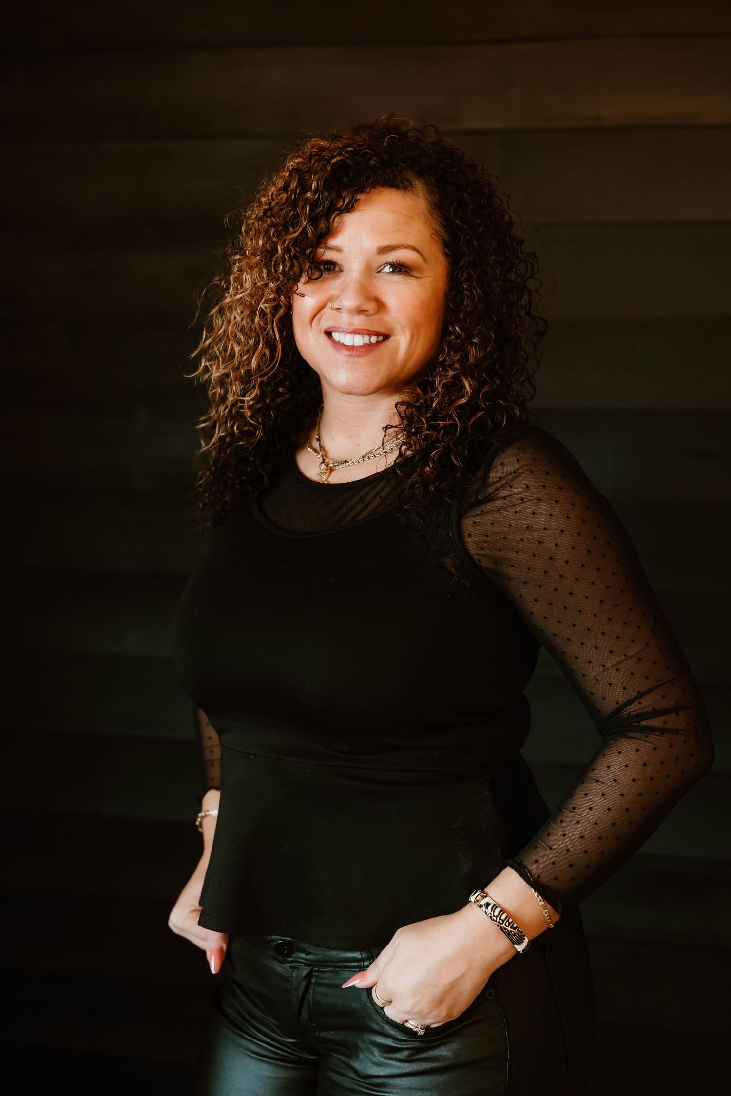 Professional in black polka dot sleeve top posing against dark background.