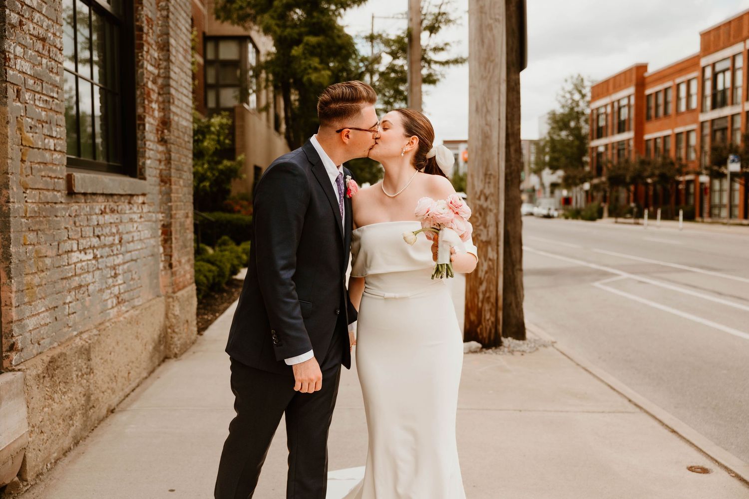 A romantic urban wedding portrait against a brick building on a city street.