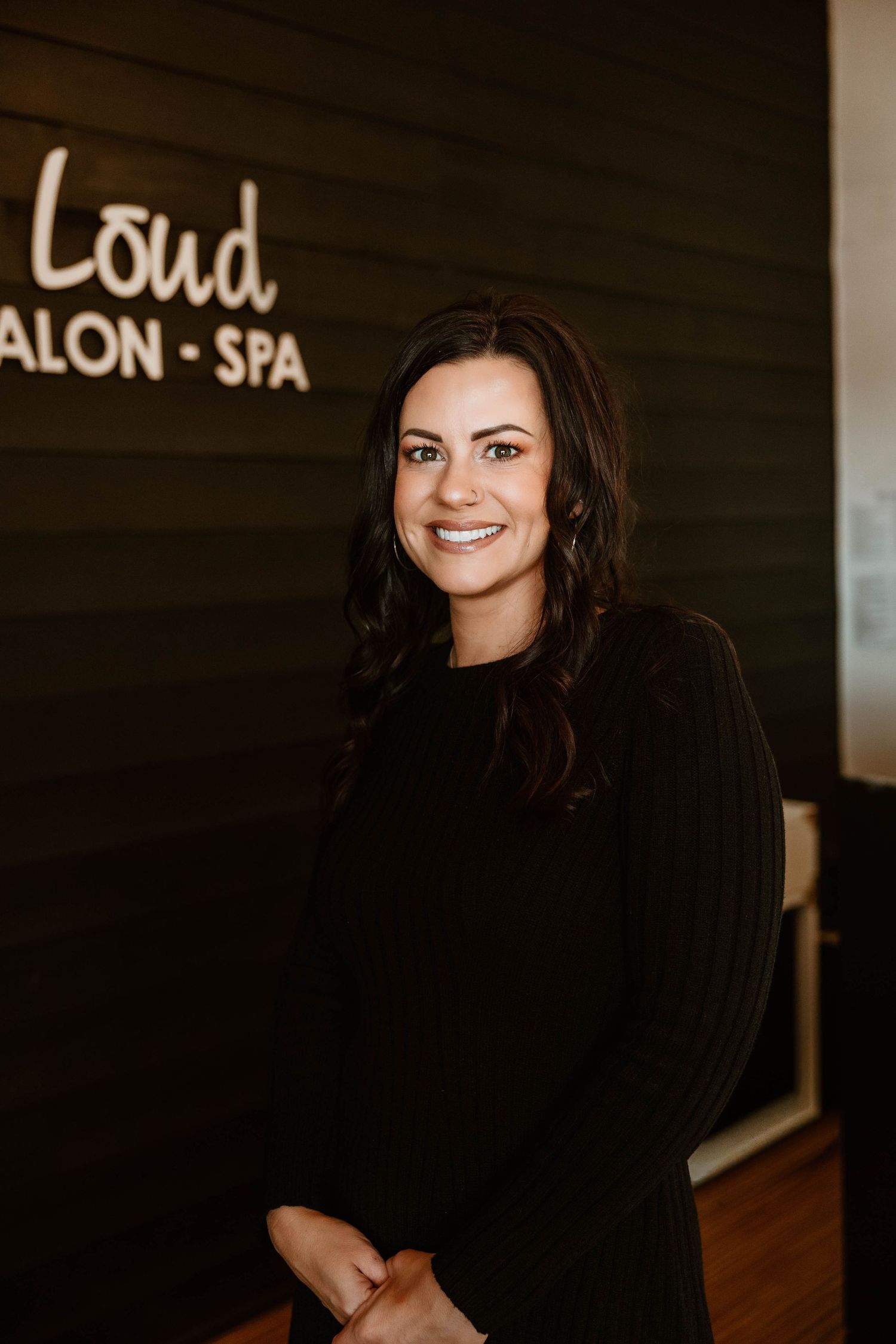 Professional salon portrait against dark wood wall with business signage visible.