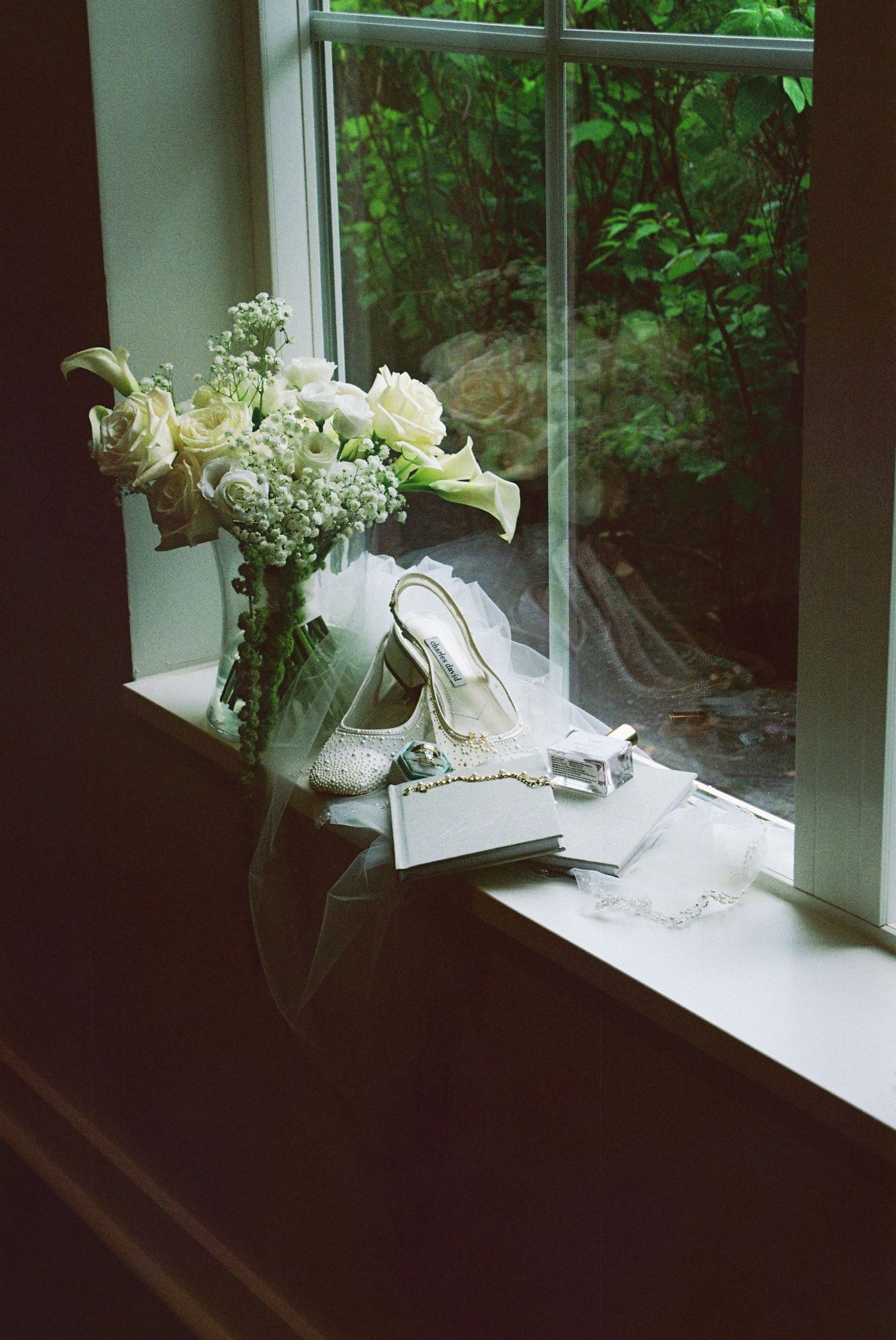Bridal accessories including white heels, bouquet, veil, and jewelry displayed on a window ledge.
