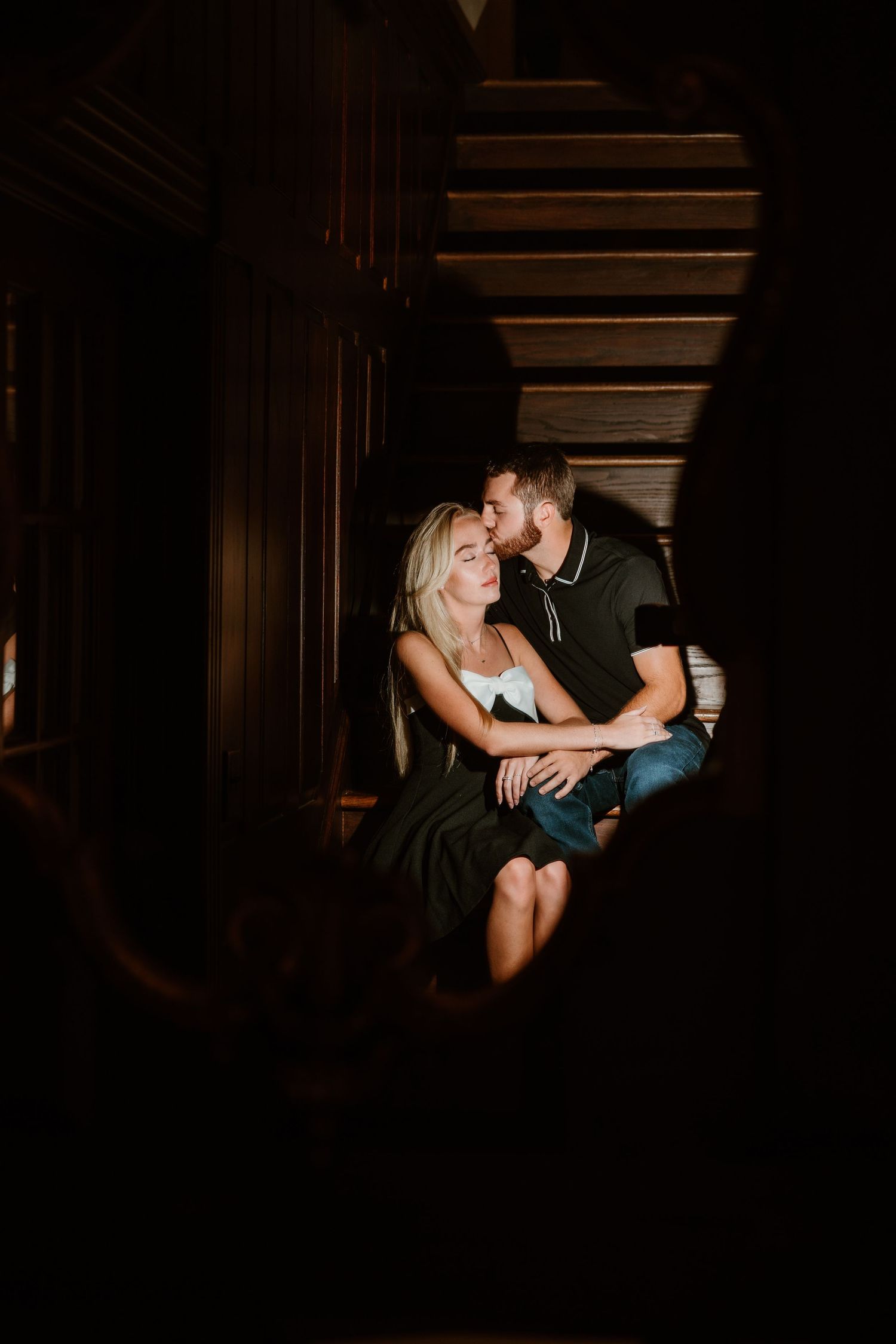 A couple shares an intimate moment in a dark wooden hallway.