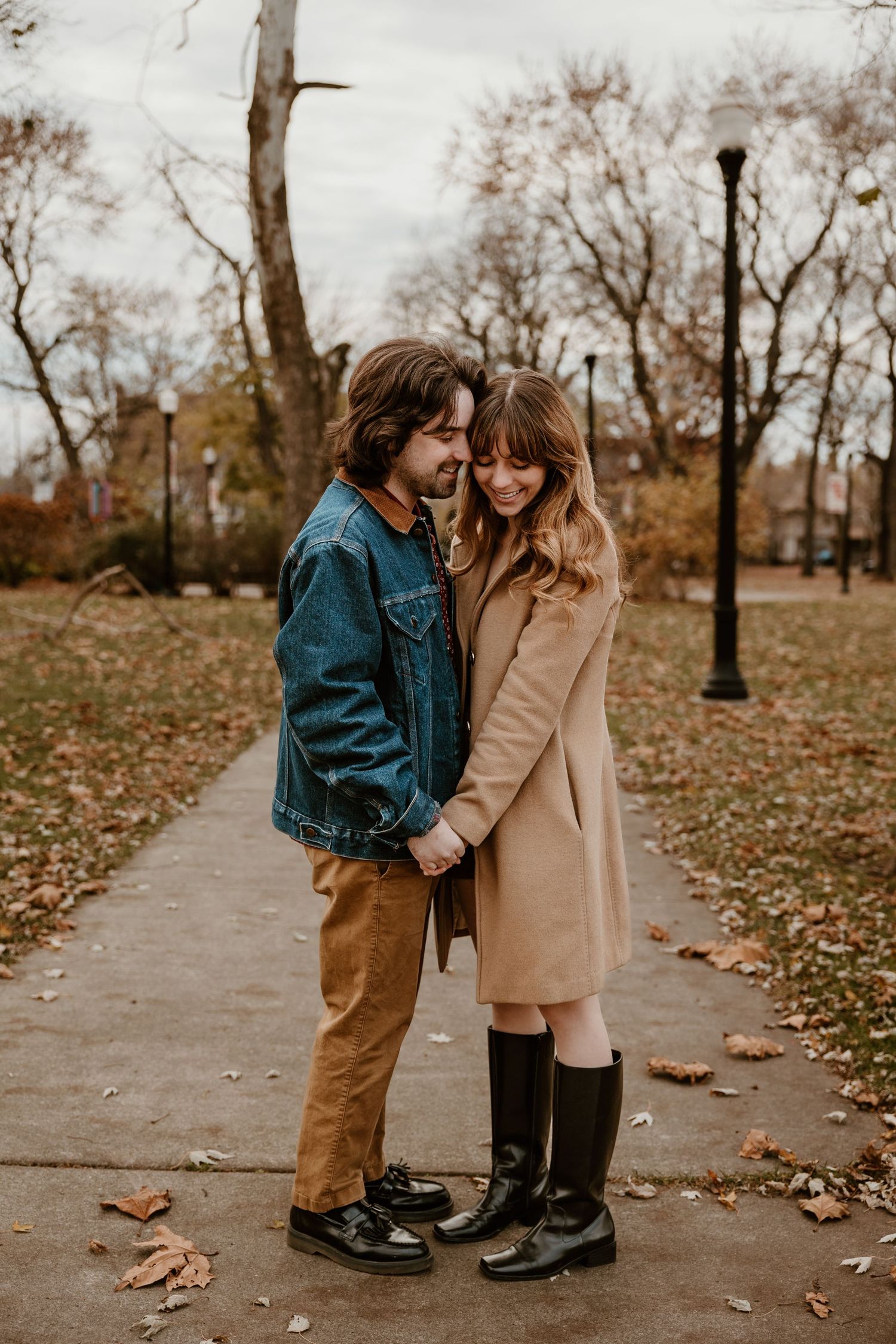 Couple in casual fall outfits share intimate moment on park pathway.