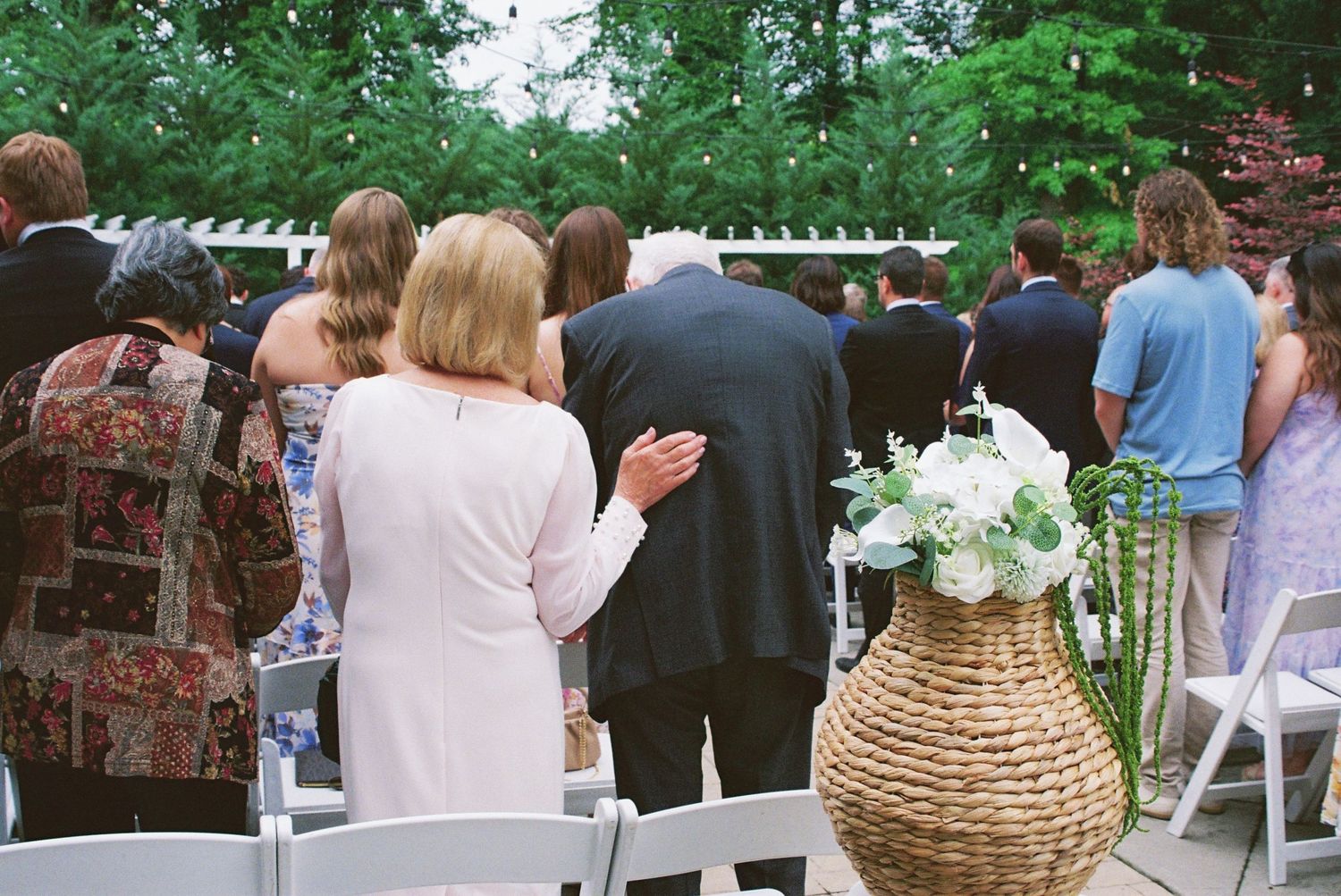 Wedding guests watching outdoor ceremony with a wicker basket of white flowers in the foreground.