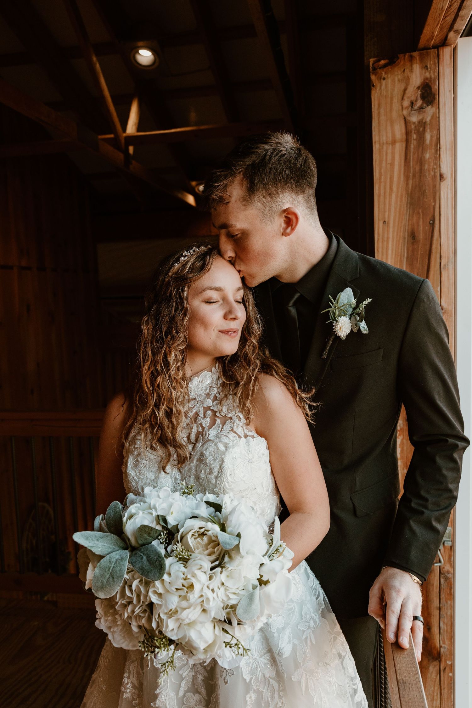 Intimate wedding portrait in rustic wooden venue with white floral bouquet.