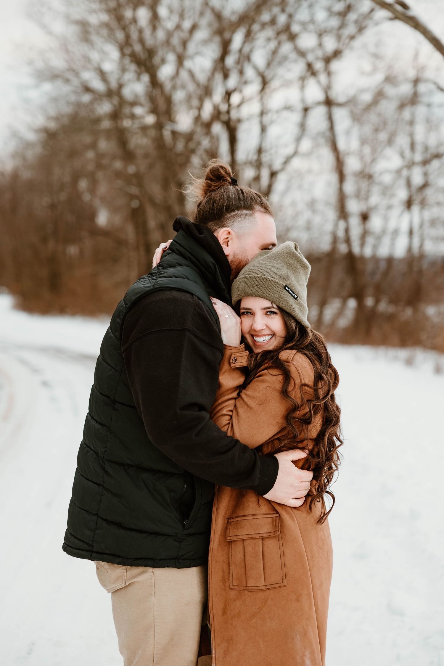 Romantic winter engagement photos with couple embracing in snowy landscape.