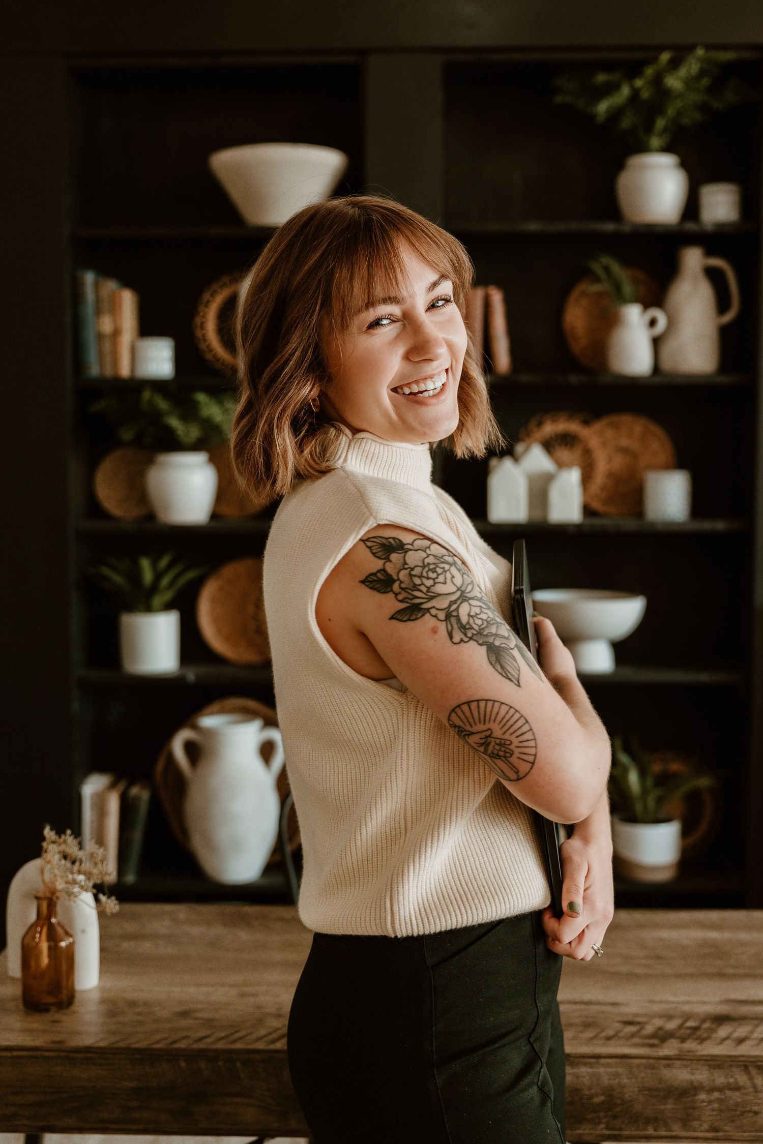 Person in cream sweater sitting on brown leather couch with decorative shelving behind.