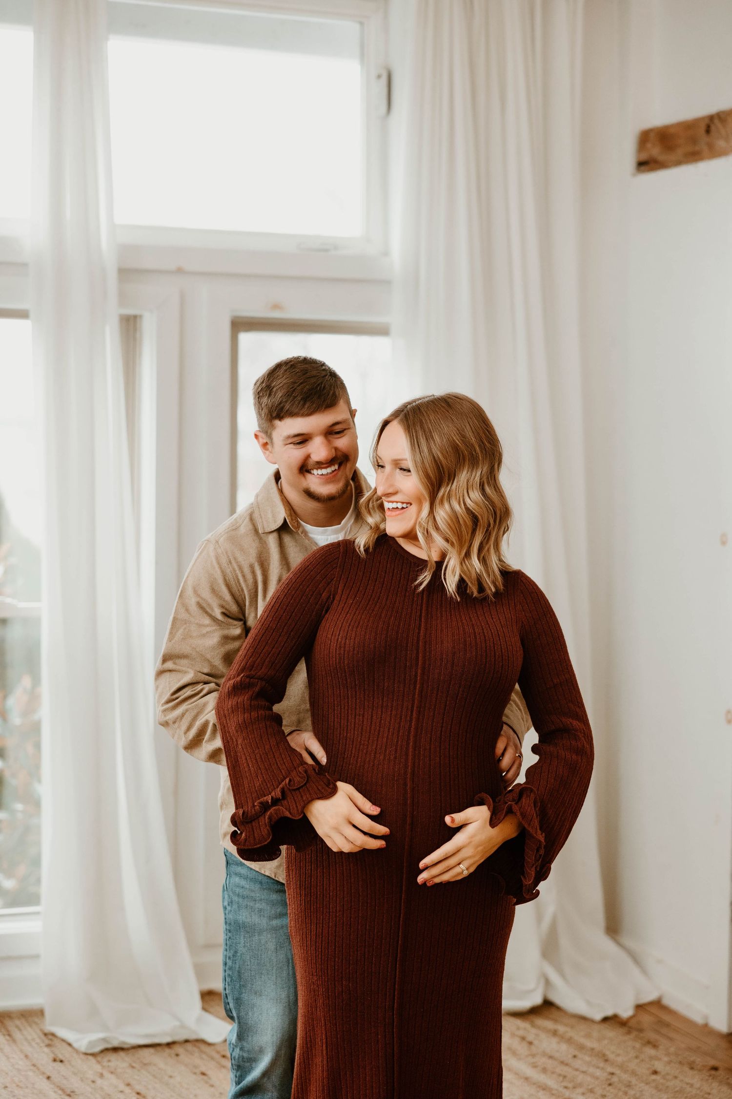Couple sharing an intimate moment in a bright sunlit room with white curtains.