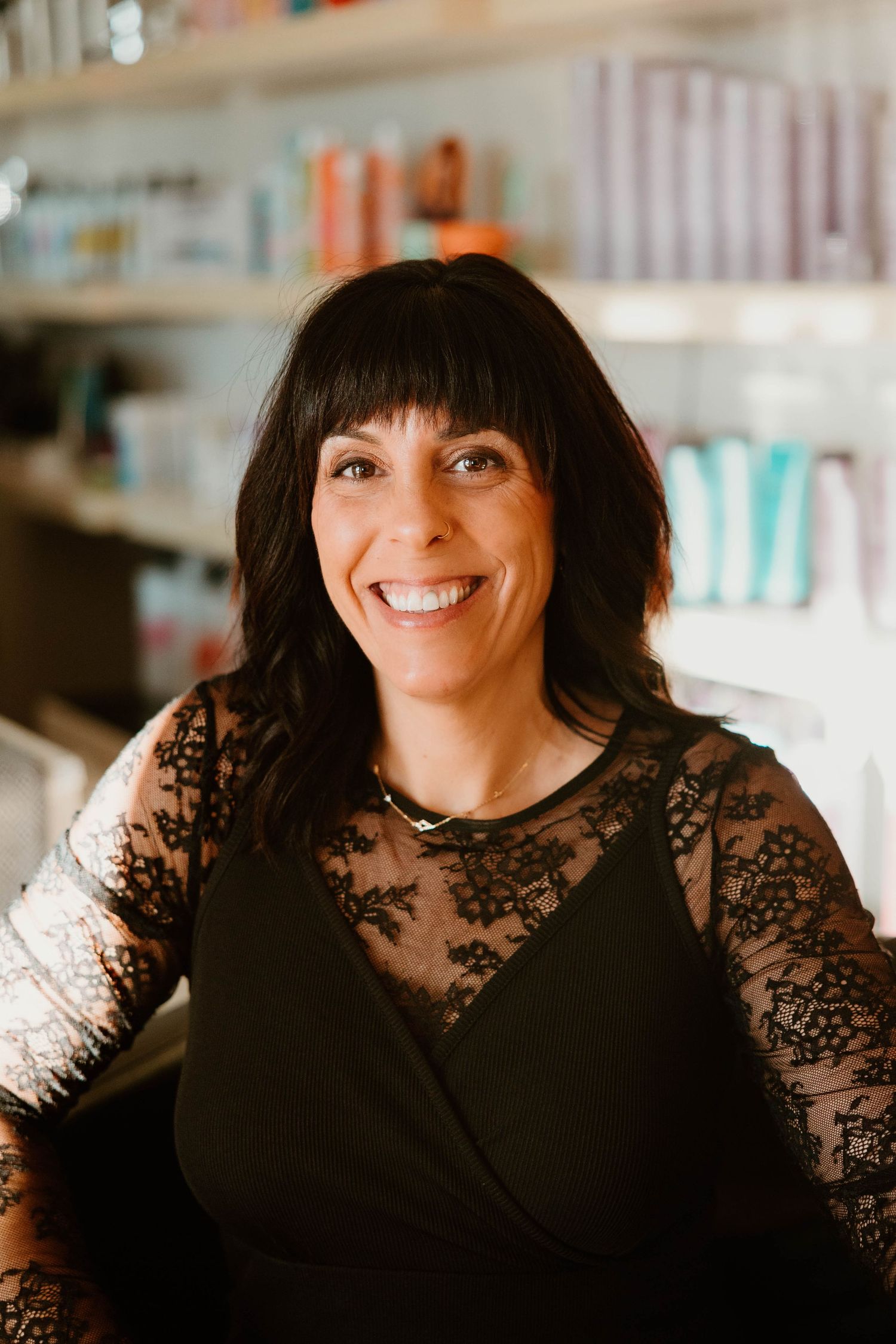Professional wearing black lace top poses with expressive smiles in salon setting.