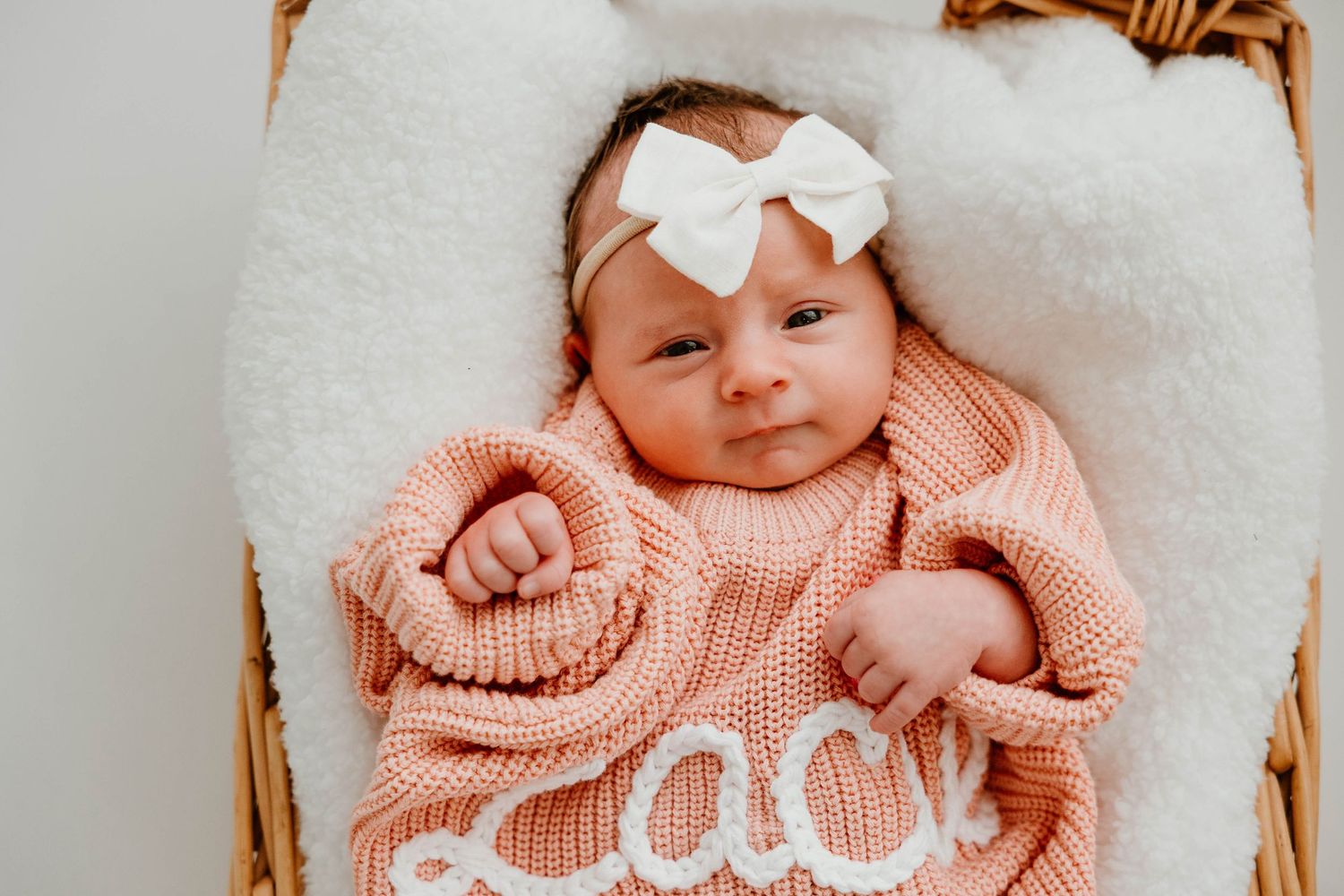 Newborn baby wearing pink knit sweater sleeping in white basket.