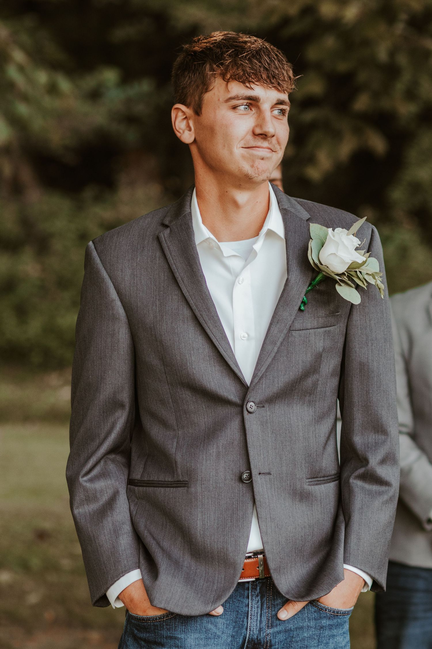 Groomsmen in grey suit jackets and jeans with white boutonnières pose casually outdoors.