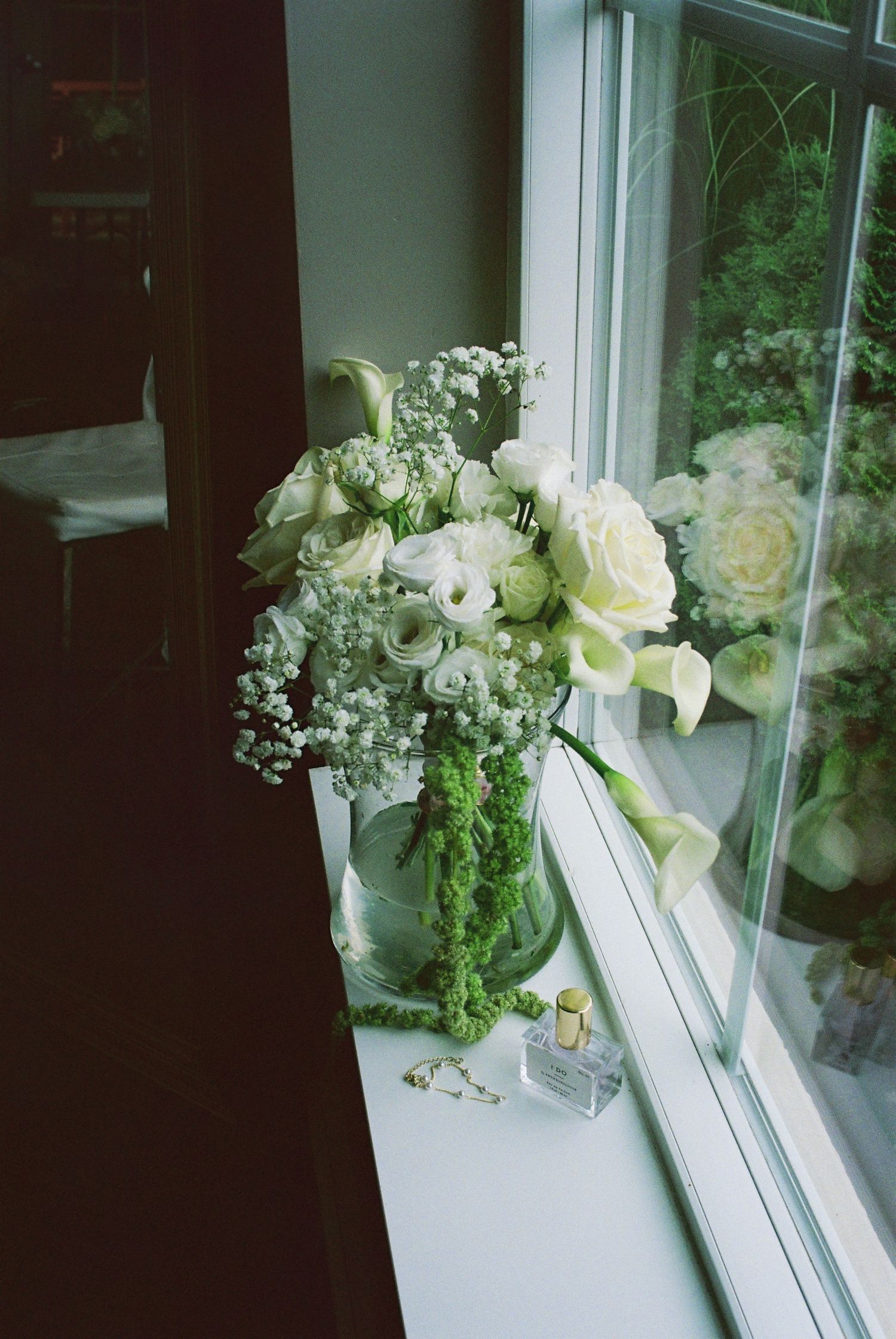 Elegant white wedding bouquet with roses and baby's breath displayed on a sunlit windowsill.