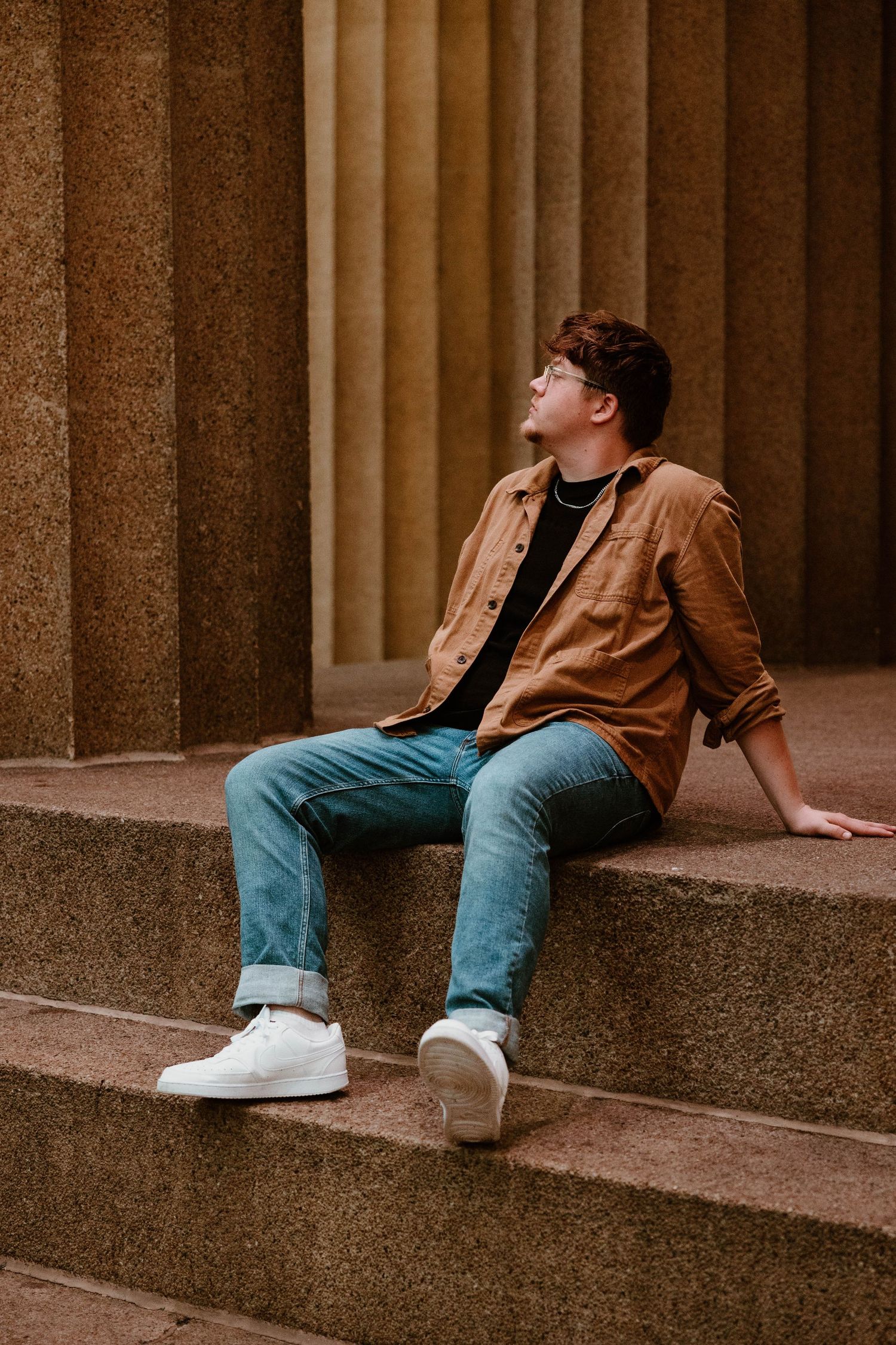 Someone in casual wear lounges on concrete steps with architectural columns in the background.