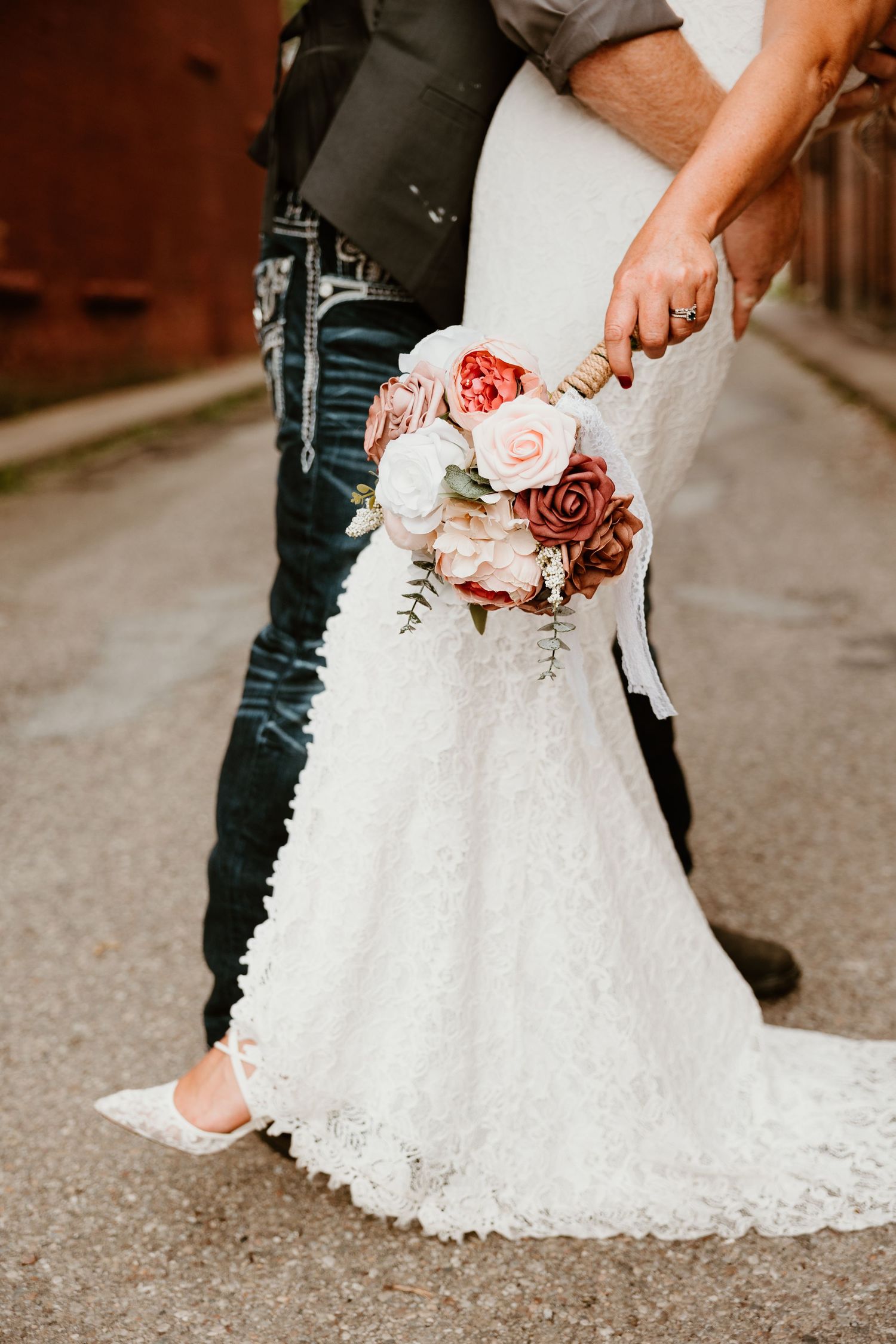 Close-up detail of a white lace wedding dress and blush rose bouquet.