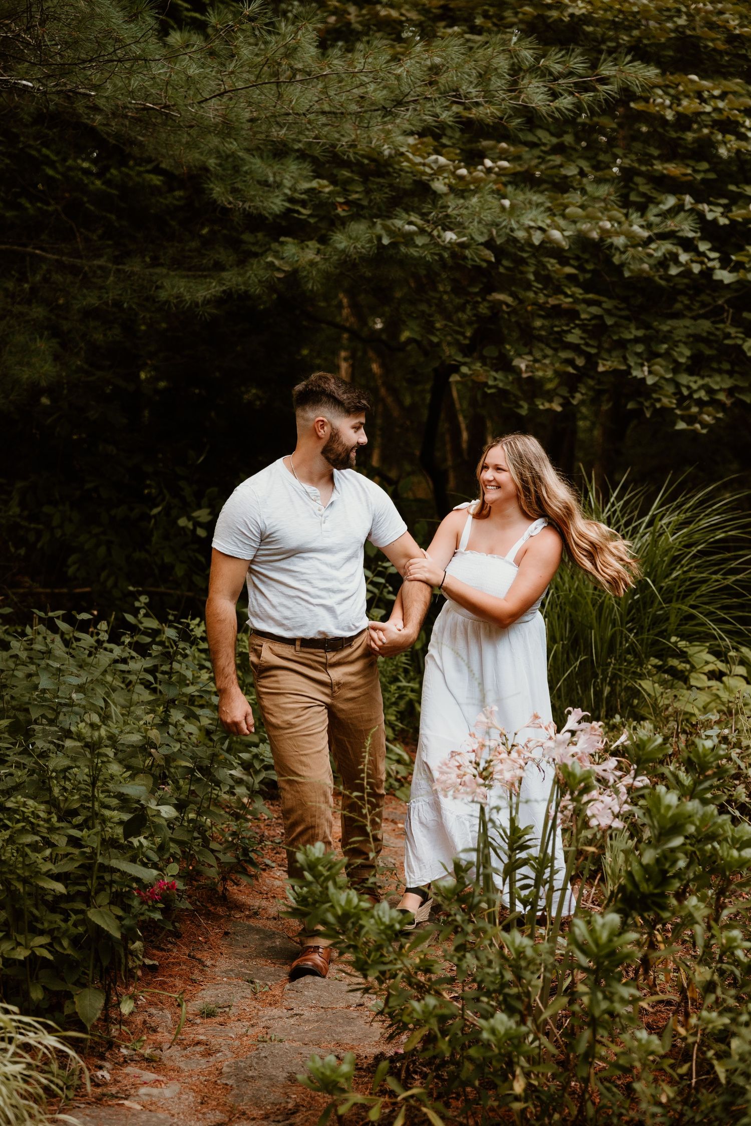 A couple walks together on a nature trail surrounded by lush greenery.