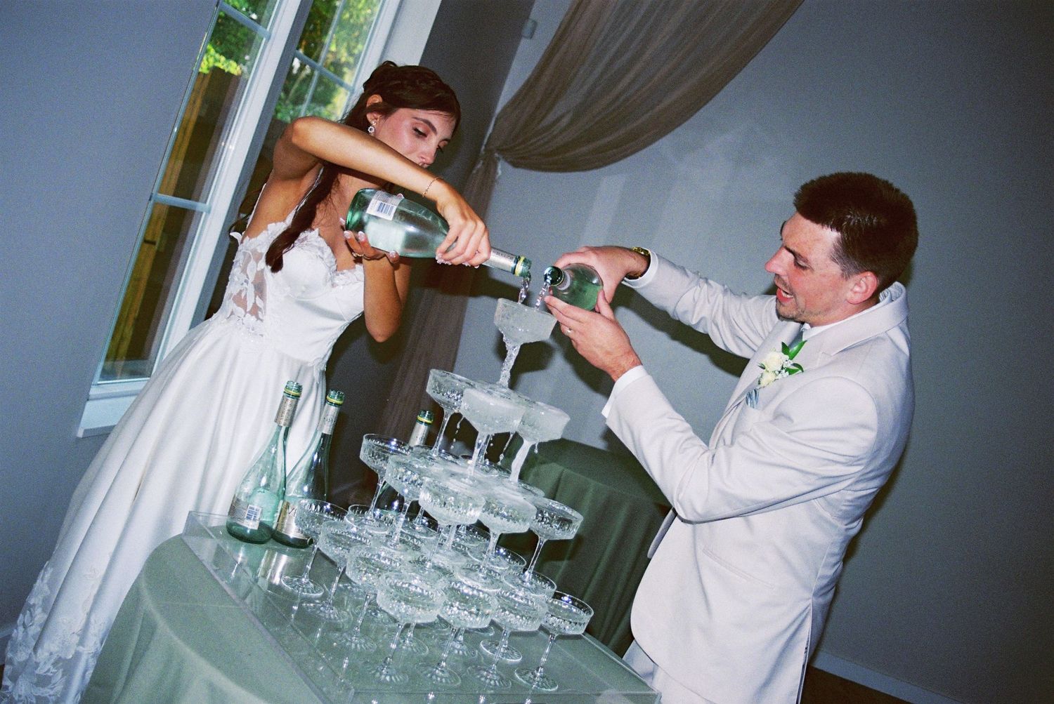 Bride and groom filling a champagne tower with glasses at their elegant wedding reception.