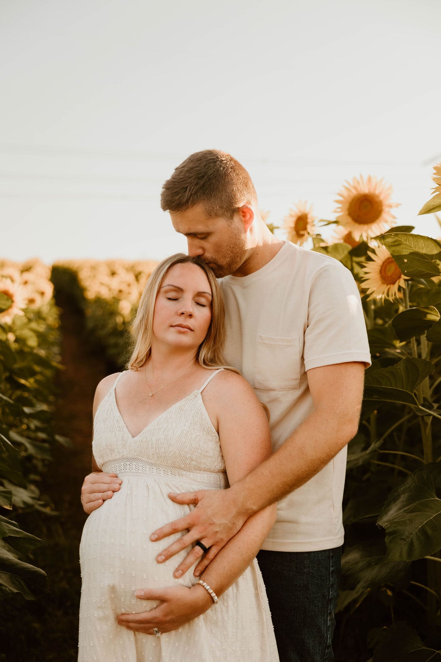Romantic maternity photos in sunflower field during golden hour sunset.