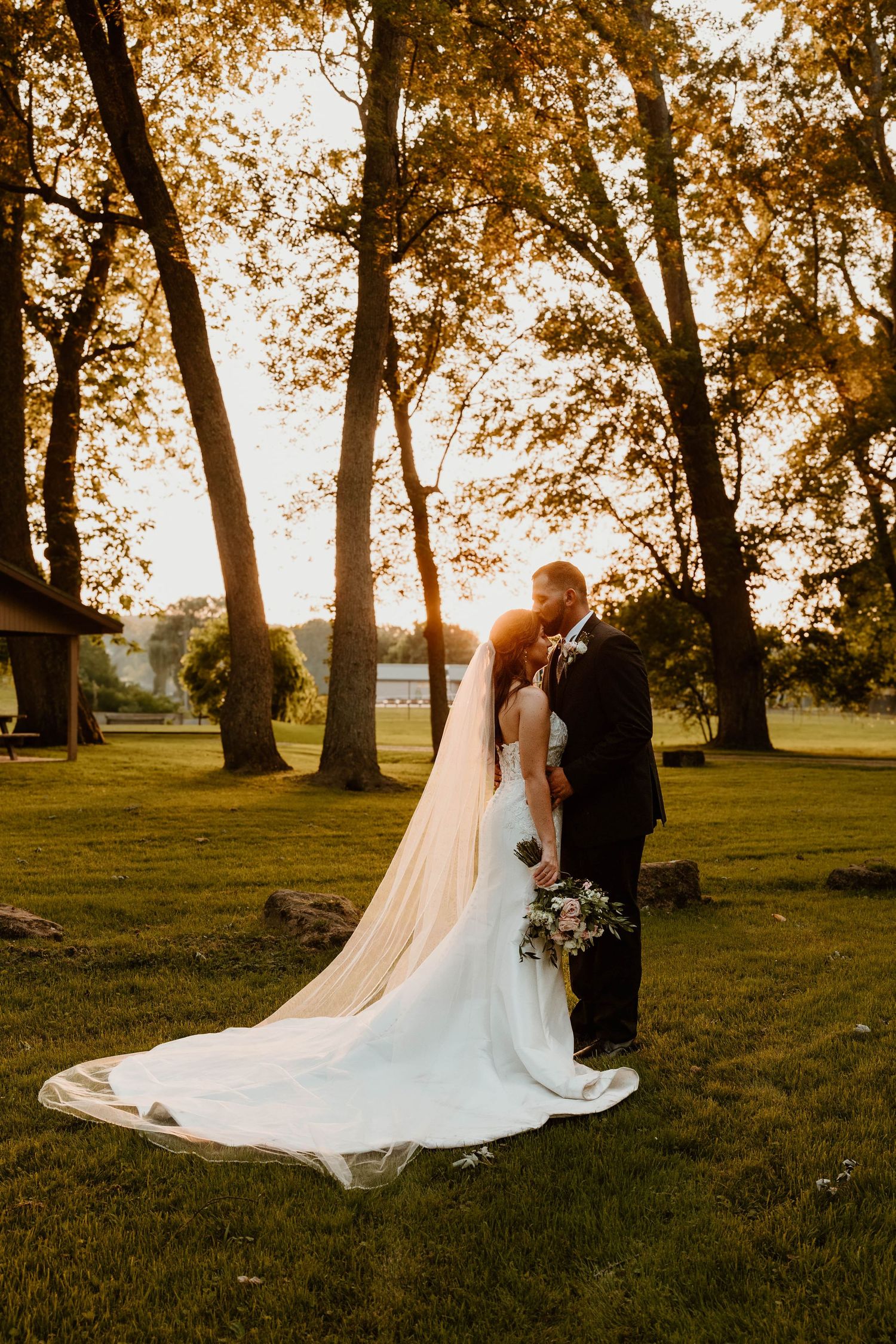Couple takes romantic sunset photos under tall trees on their wedding day.