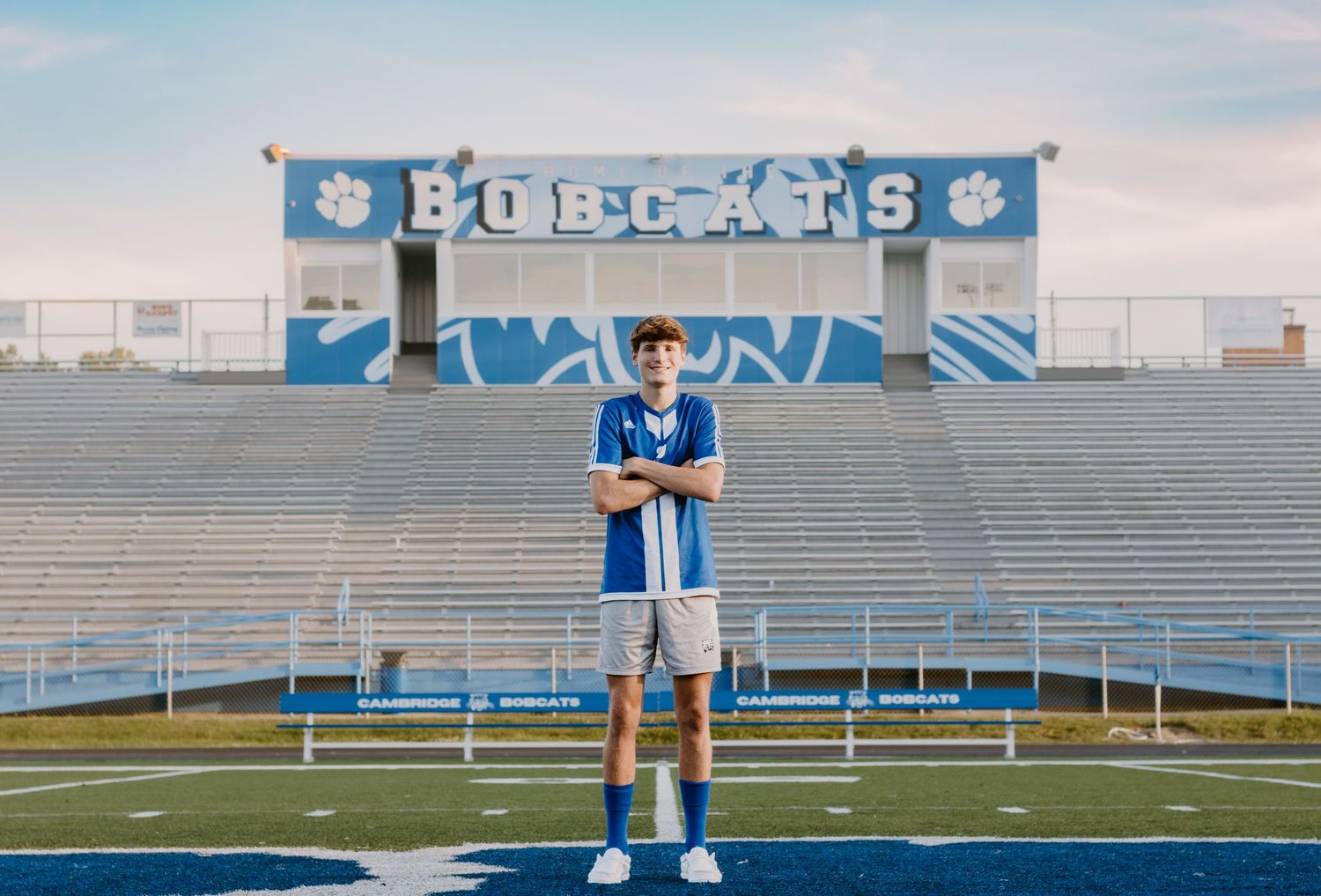 Empty high school football stadium with blue bleachers and Bobcats banner.