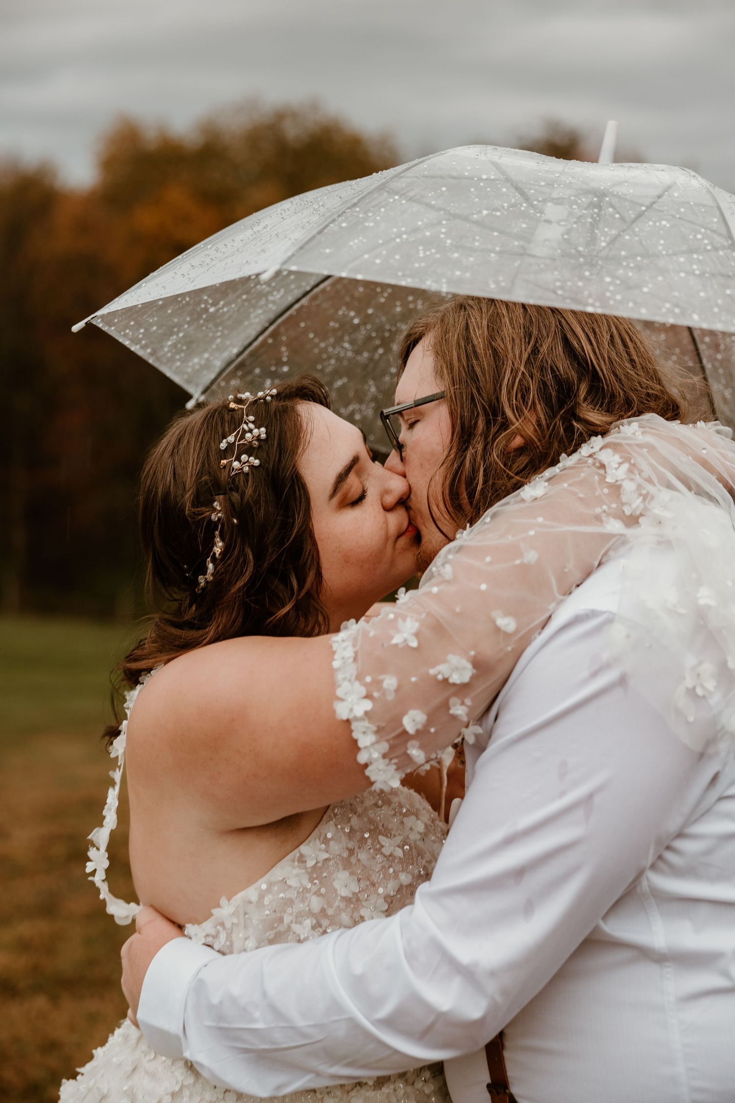 Romantic moment under clear umbrella during autumn wedding photoshoot.