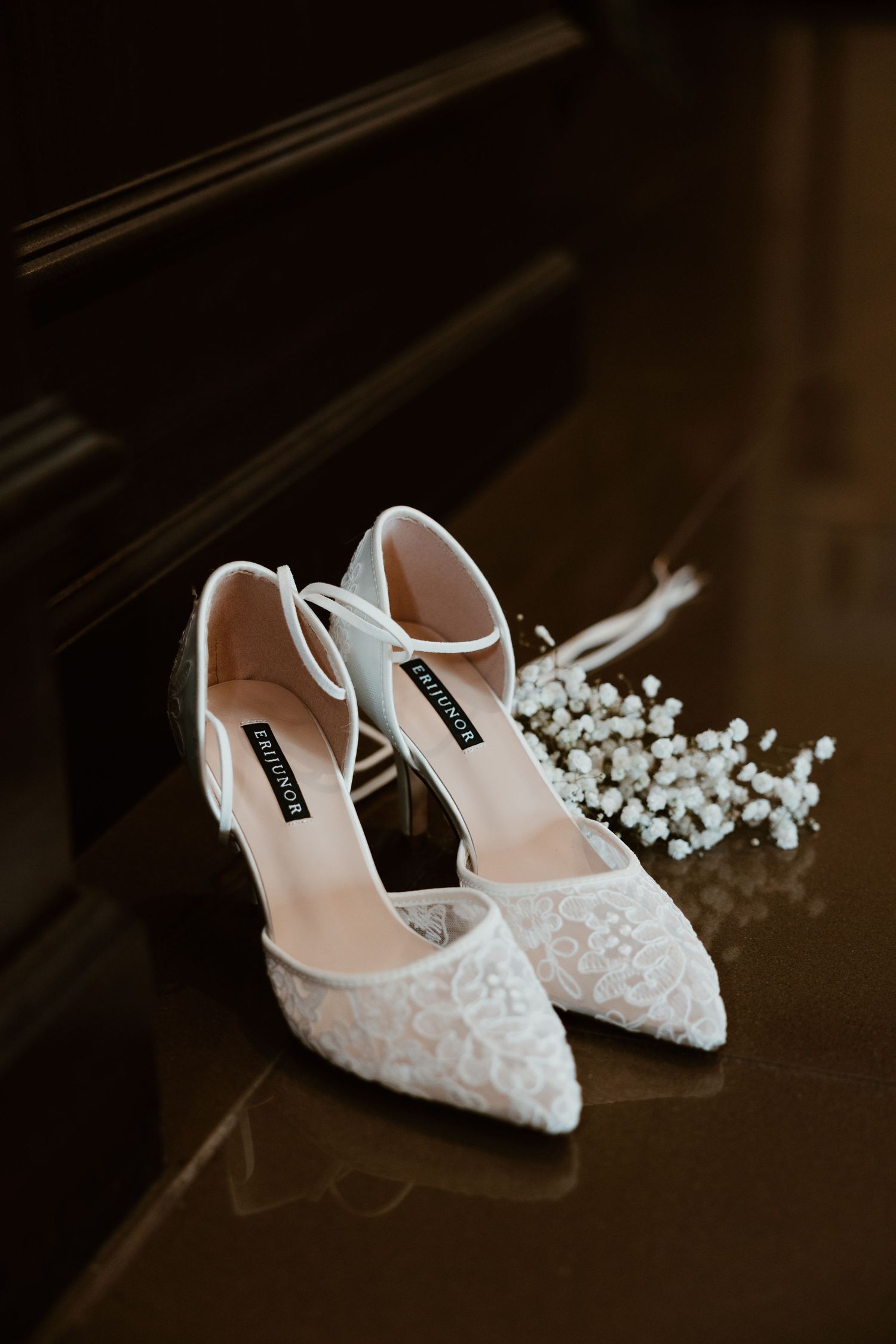 Elegant white lace bridal shoes with delicate details displayed on a dark surface.
