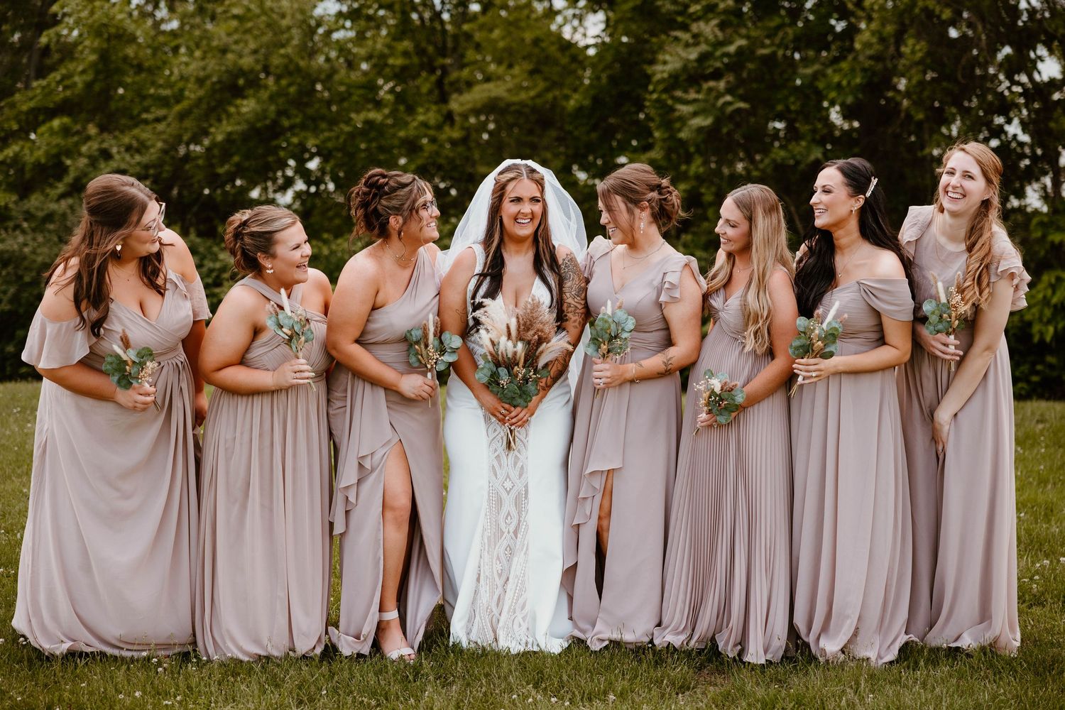 Bridesmaids in soft pink dresses pose together in an outdoor wedding setting.
