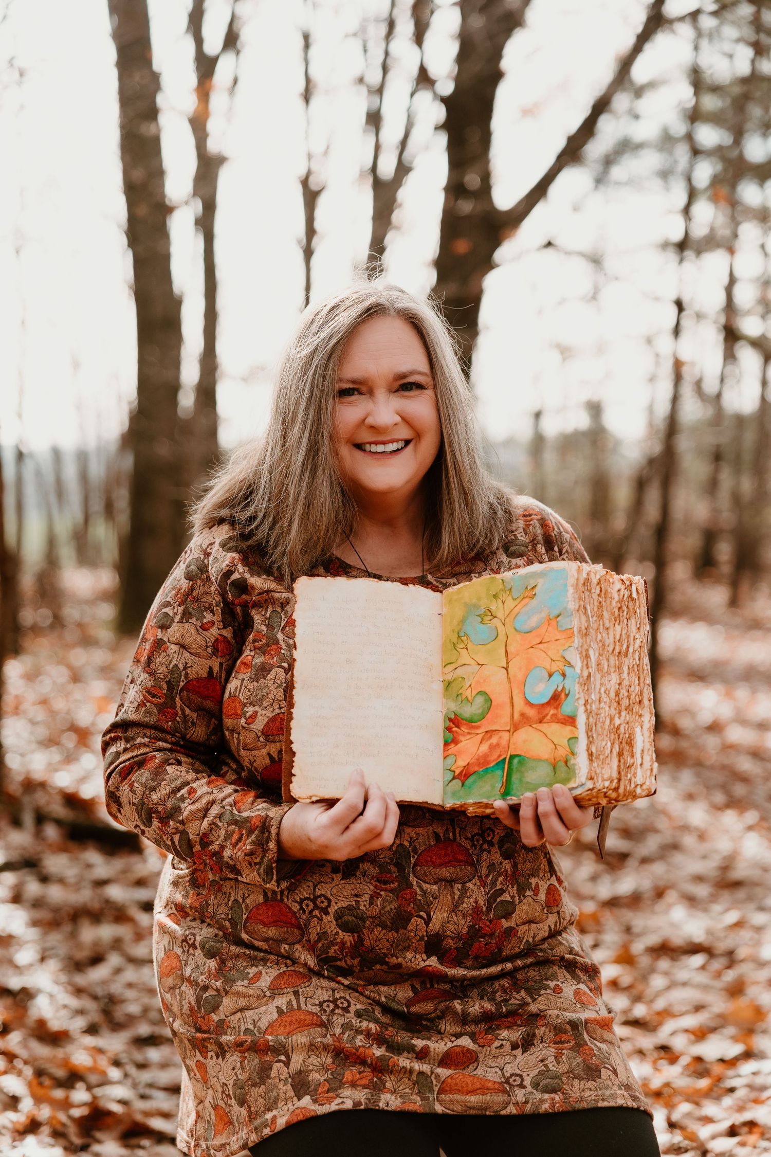 Person in floral top holding painted wooden artwork outdoors among fall leaves.