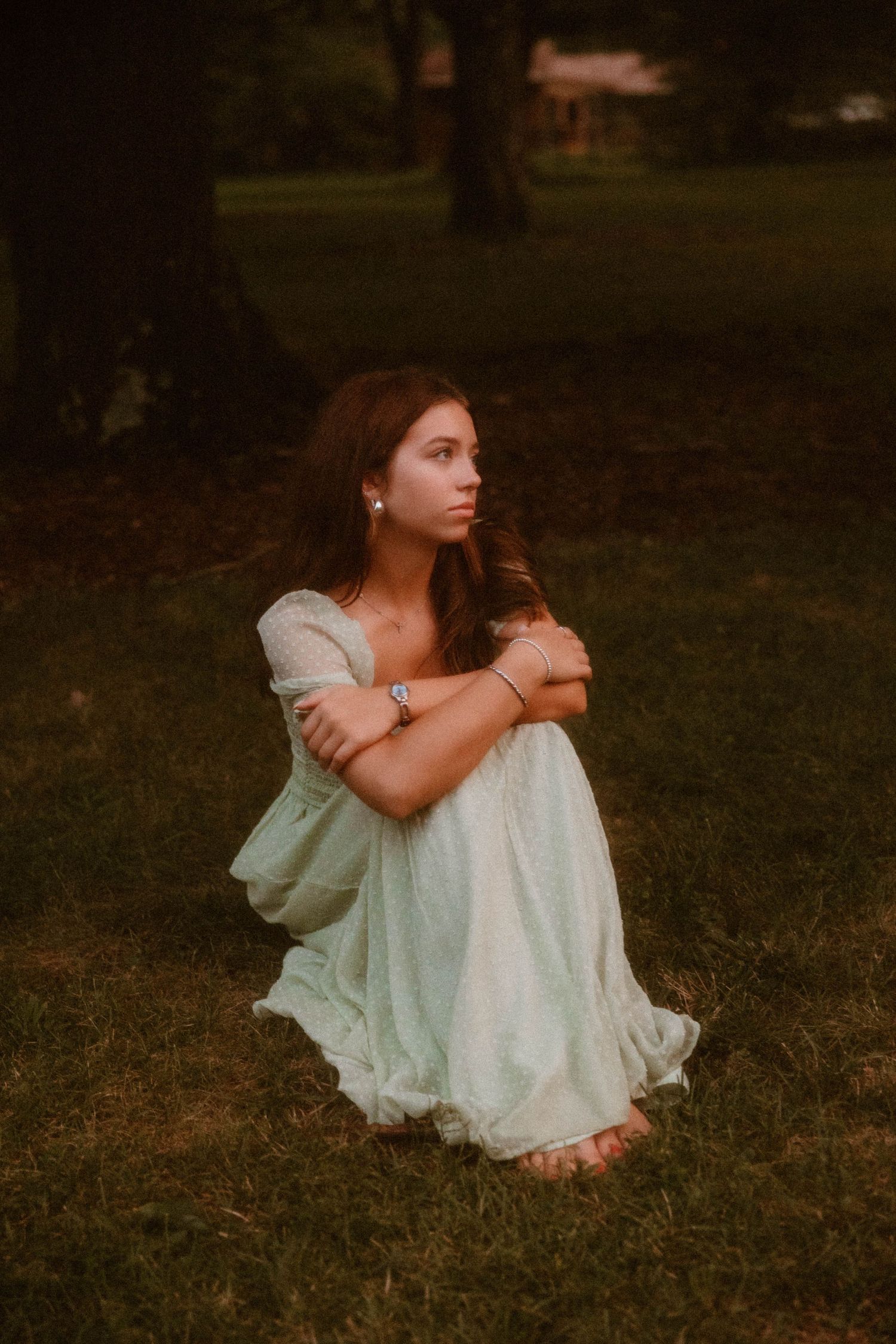 An artistic portrait of someone in a vintage-style dress sitting on grass at dusk.