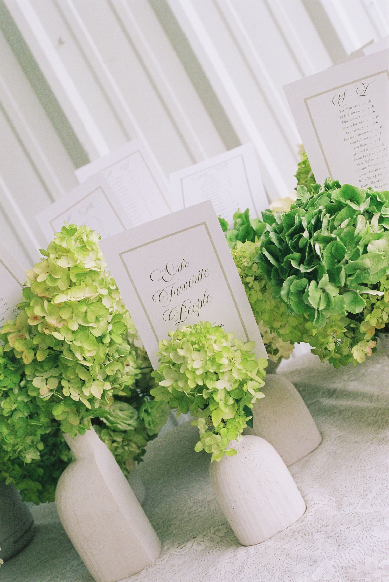 Green hydrangea centerpieces in white vases with elegant calligraphy cards on a decorated wedding reception table.