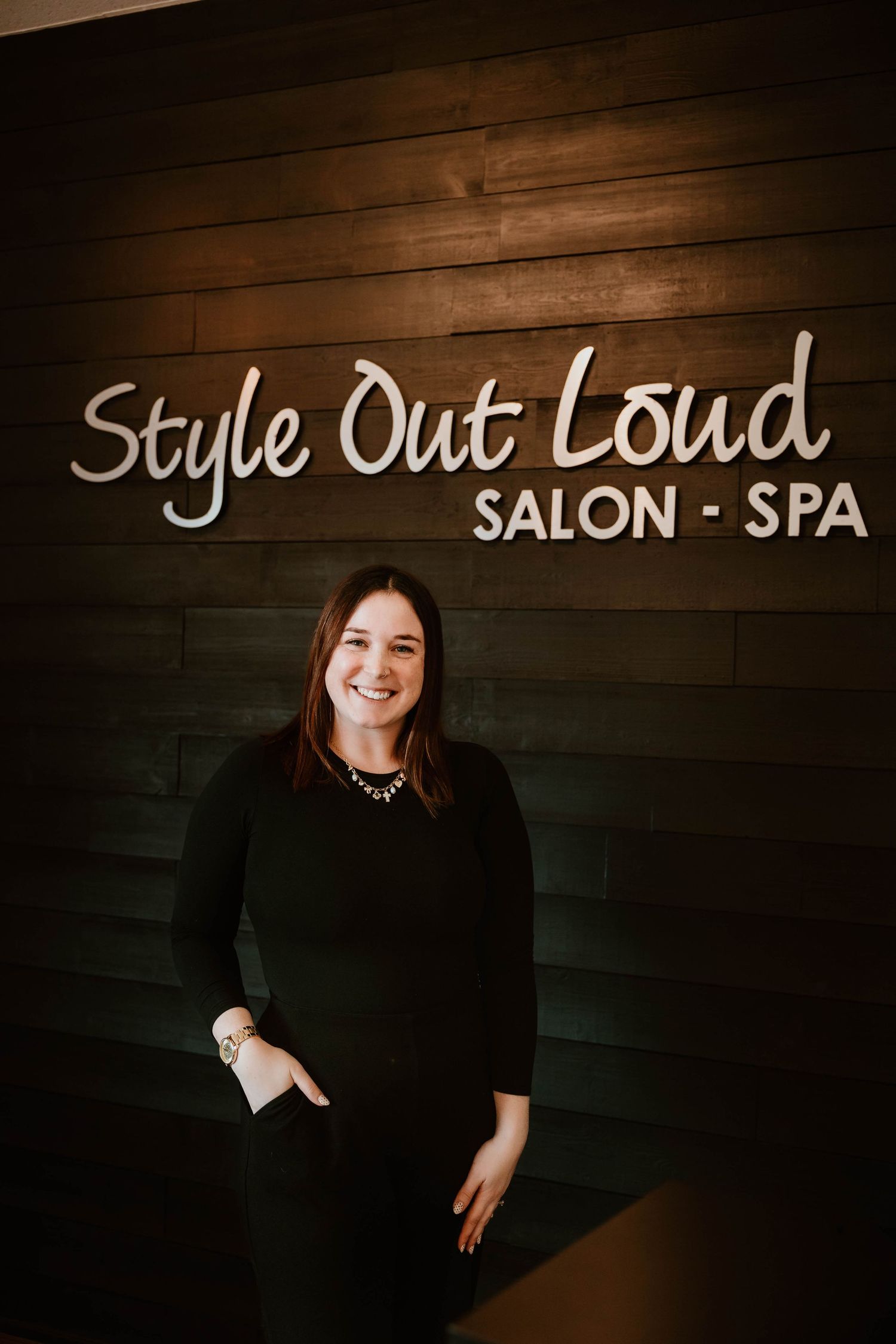 Professional salon branding photo against dark wood wall with 'Style Out Loud Salon-Spa' signage.