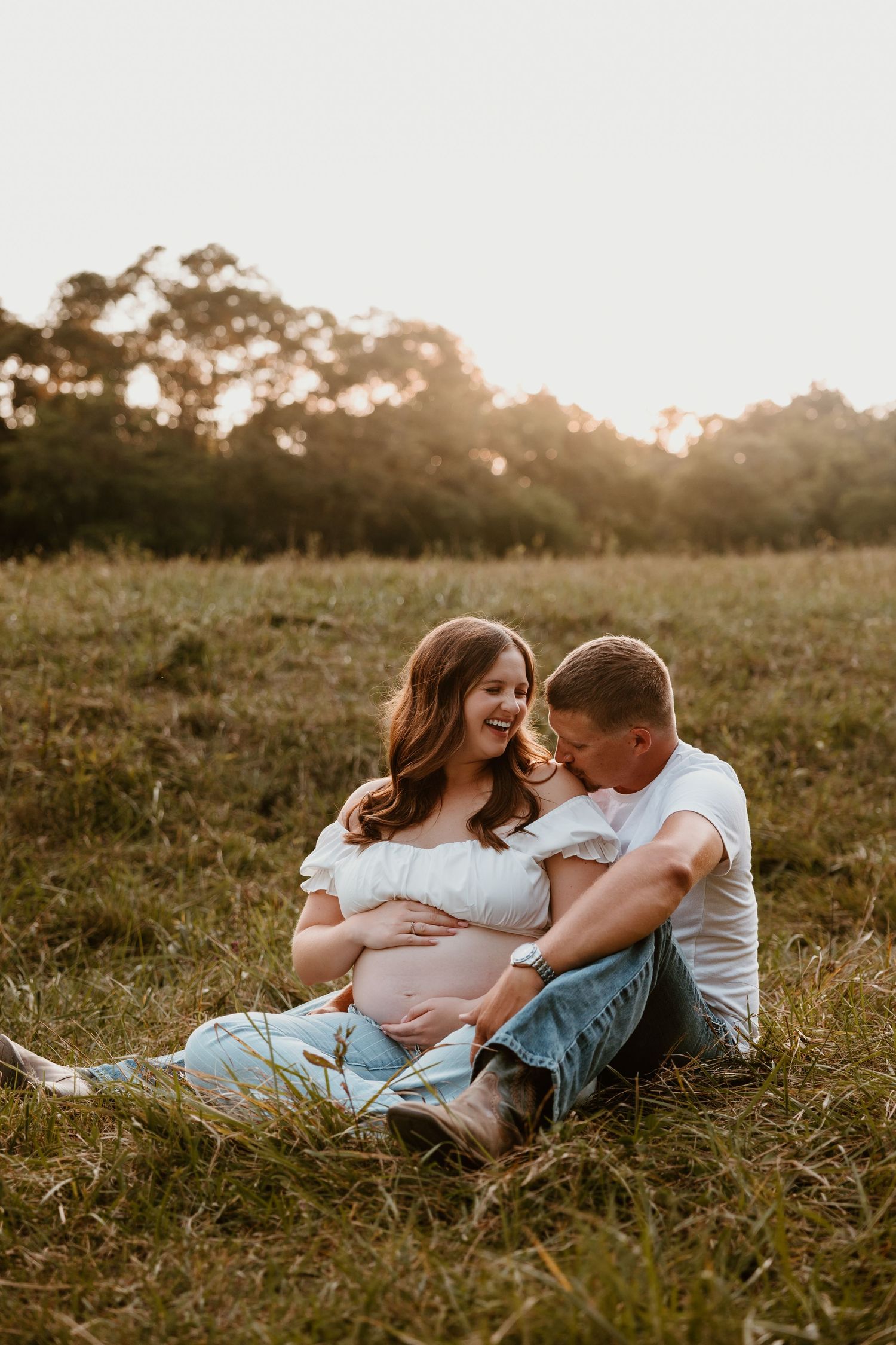 A couple relaxes in a grassy field during their sunset maternity photoshoot.