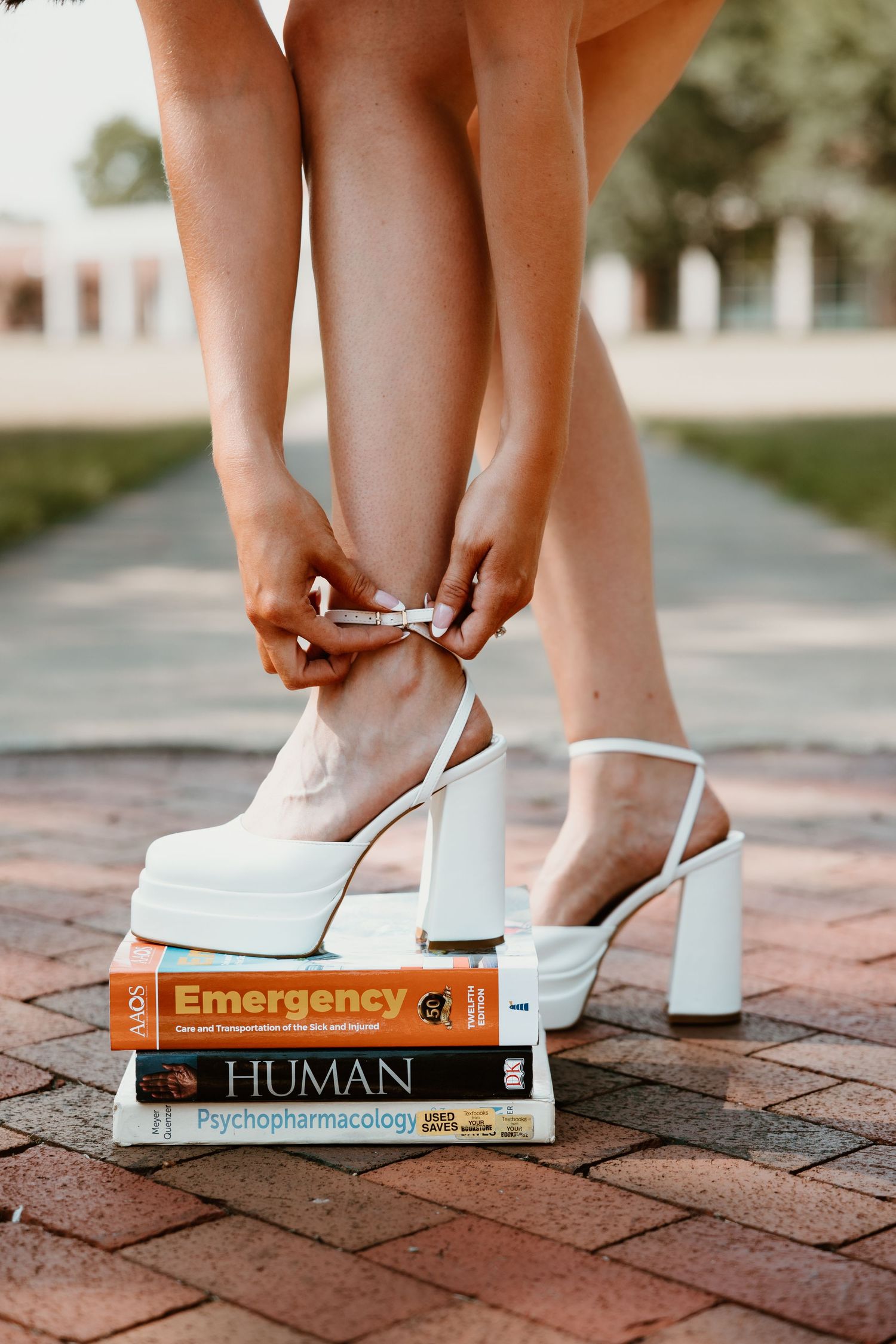 White shoes rest on top of stacked textbooks on a brick pathway.