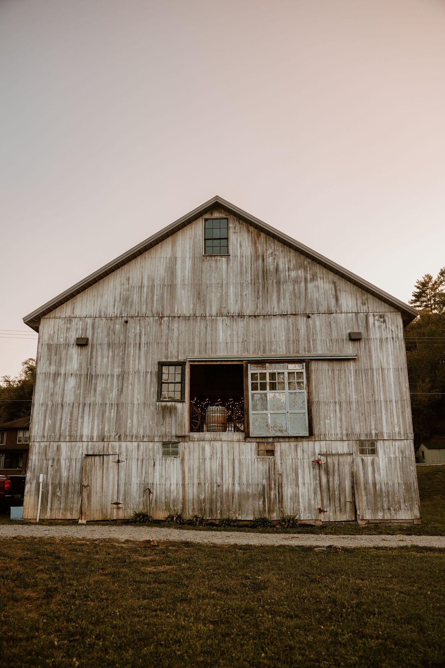 Weathered white barn exterior photographed in warm evening light shows rustic wedding venue.