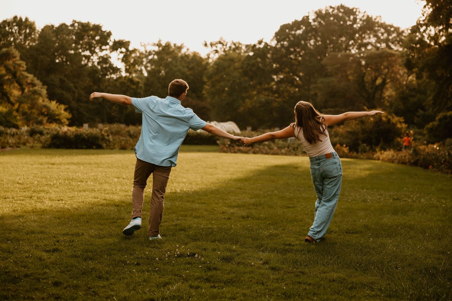 Silhouettes of people dancing playfully in a sunlit field at golden hour.