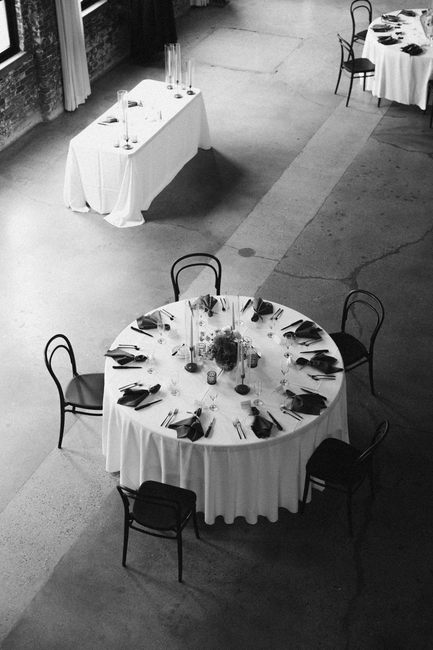 Black and white photo of elegant wedding reception tables with round settings and centerpieces.