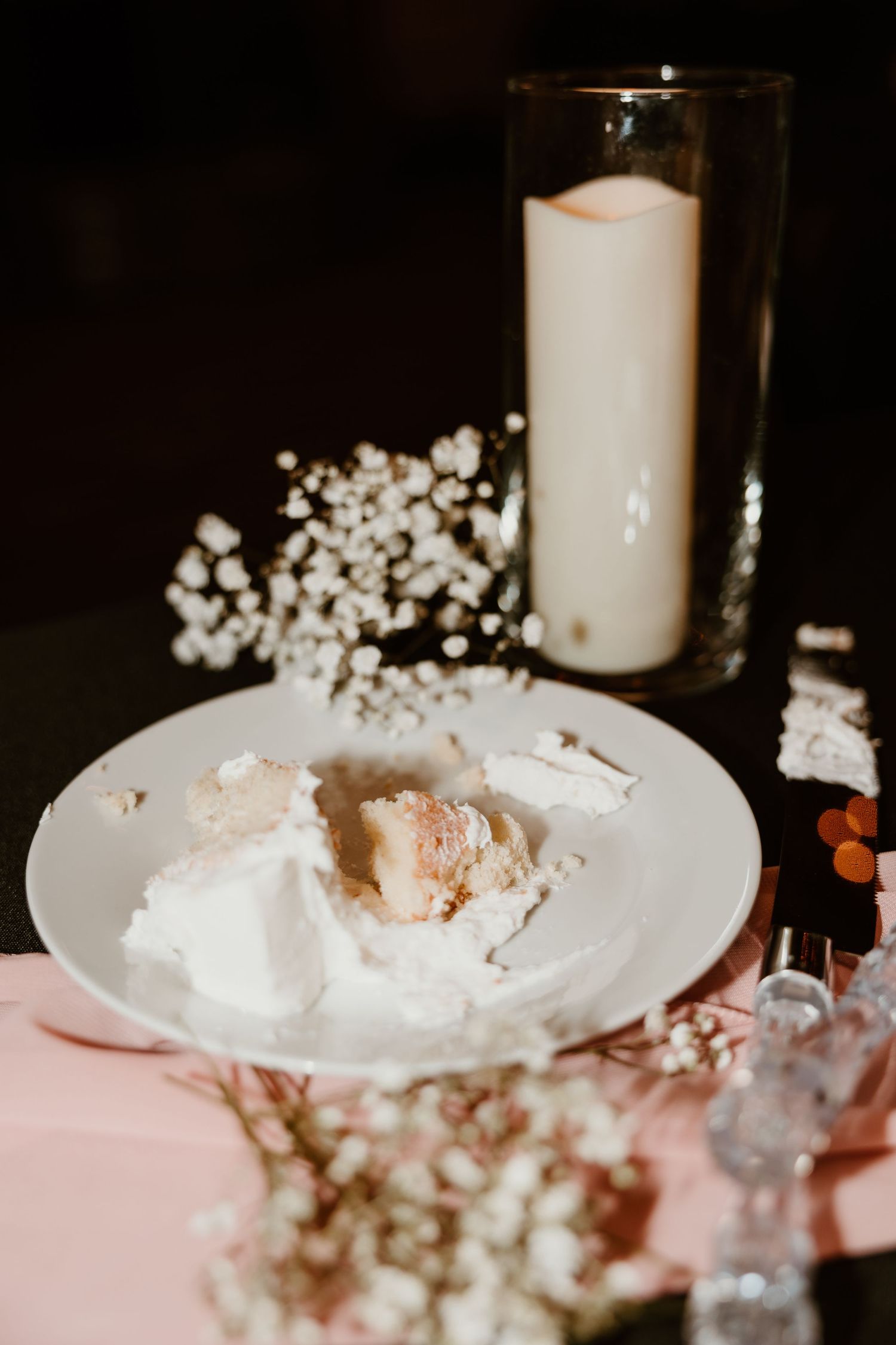 White candles and baby's breath create a romantic centerpiece on a pink tablecloth.