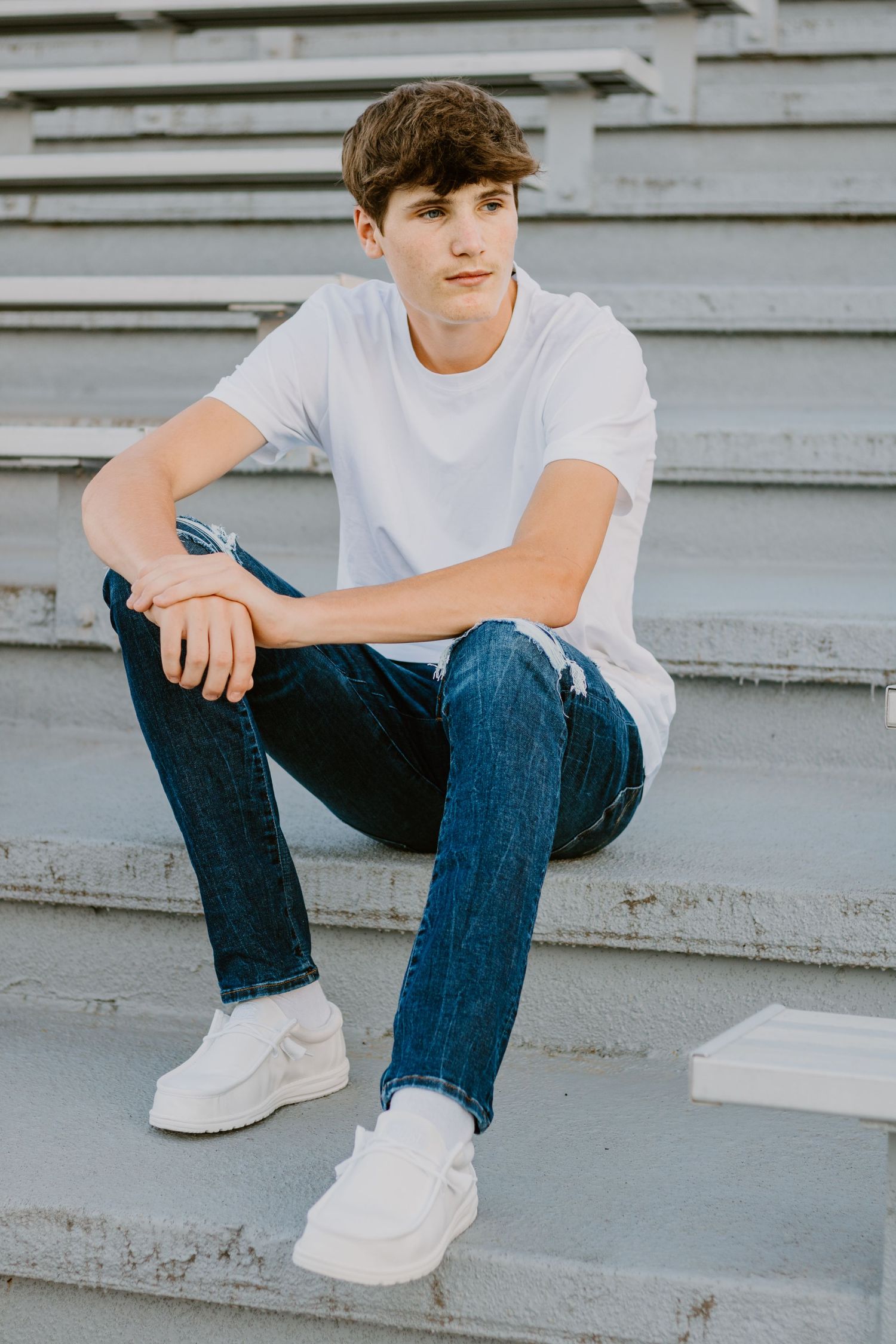Senior portrait on concrete bleachers wearing casual white t-shirt and jeans.