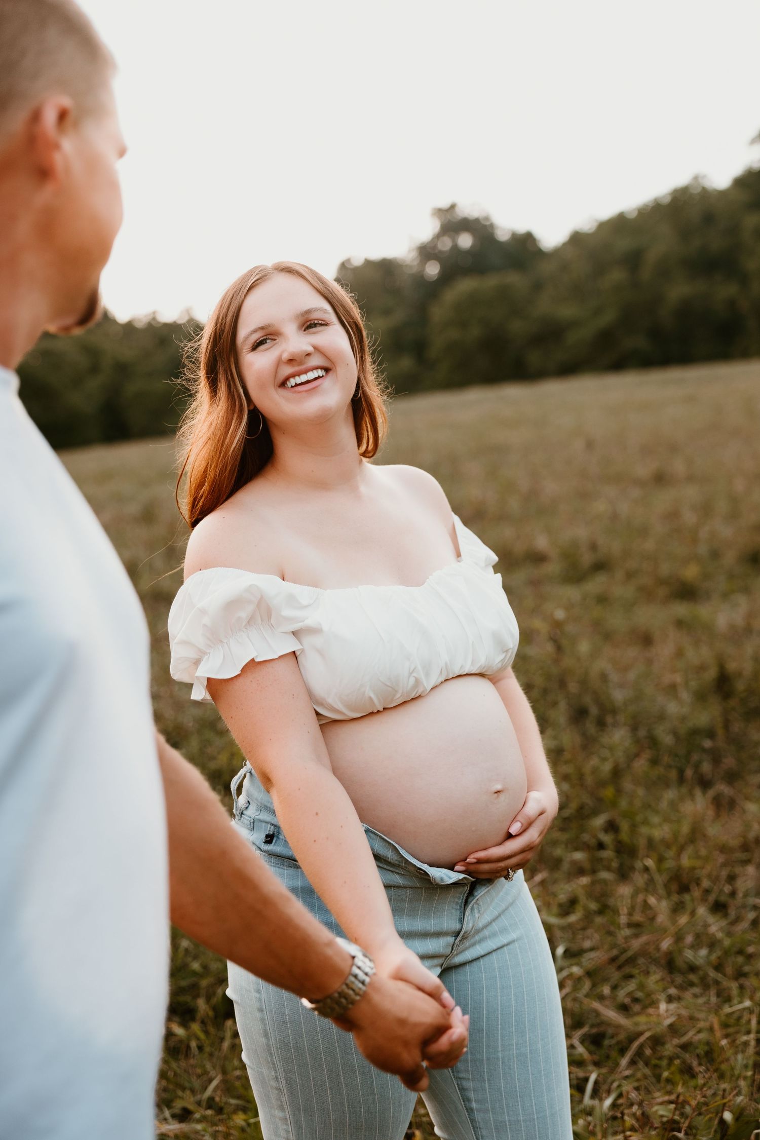 An intimate maternity moment captured in warm sunset lighting with a couple in casual attire.