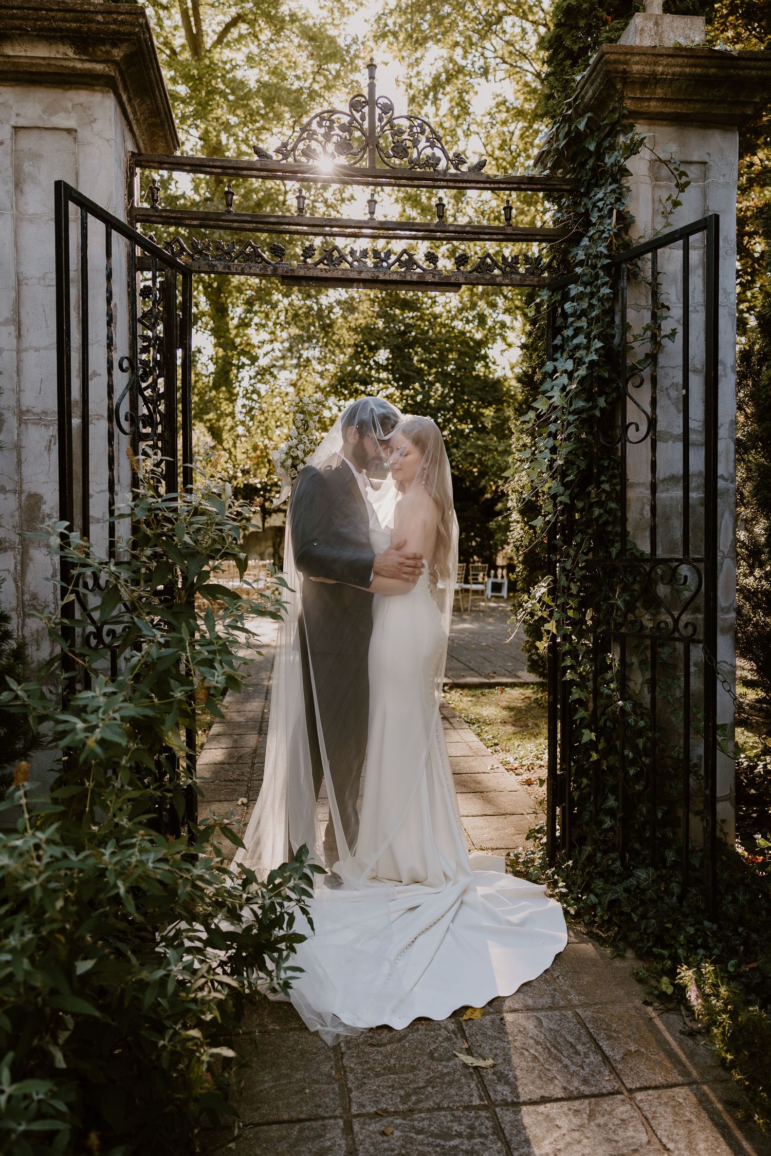 Wedding couple shares intimate moment in garden pathway with ivy covered walls.