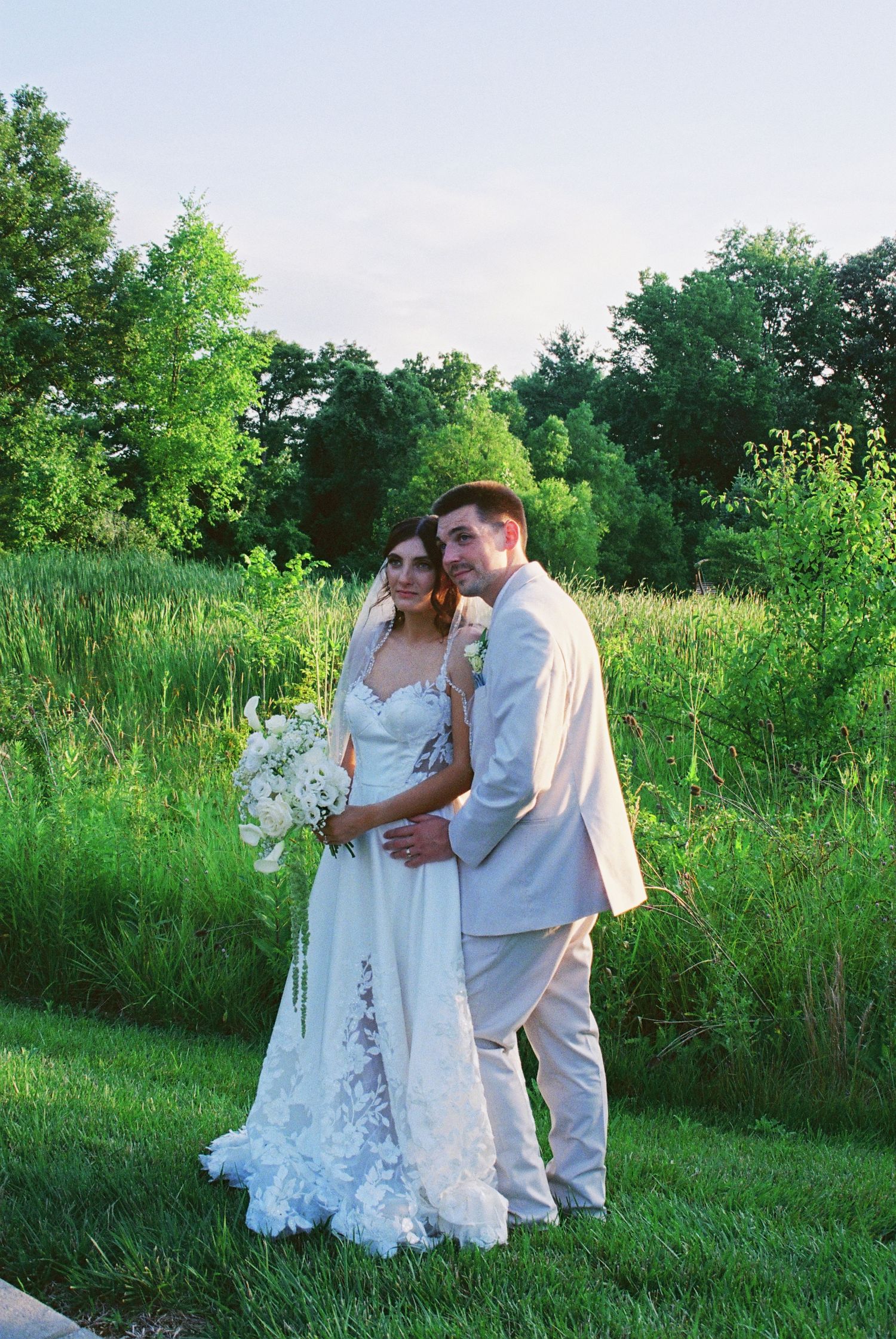 Bride and groom share romantic pose in lush green outdoor setting at golden hour.