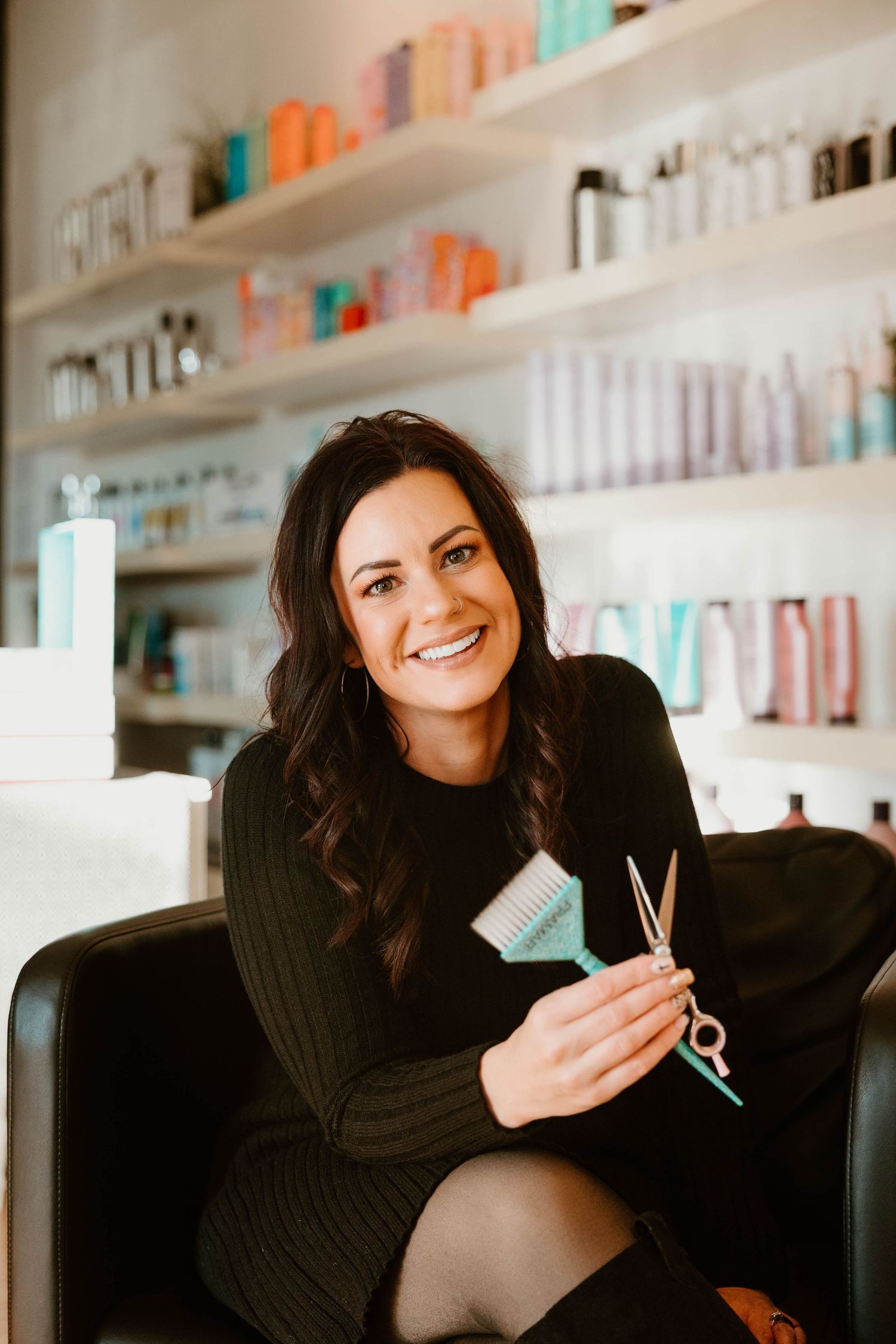 Hair stylist holding scissors in modern salon with product shelves in background.