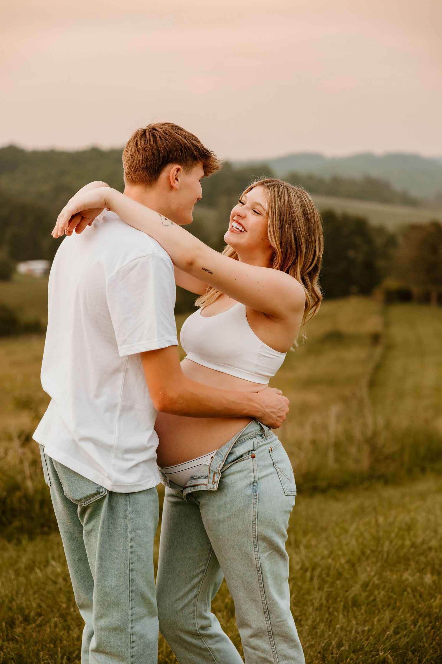 Two people in coordinated outfits share an intimate moment in a golden-lit meadow.