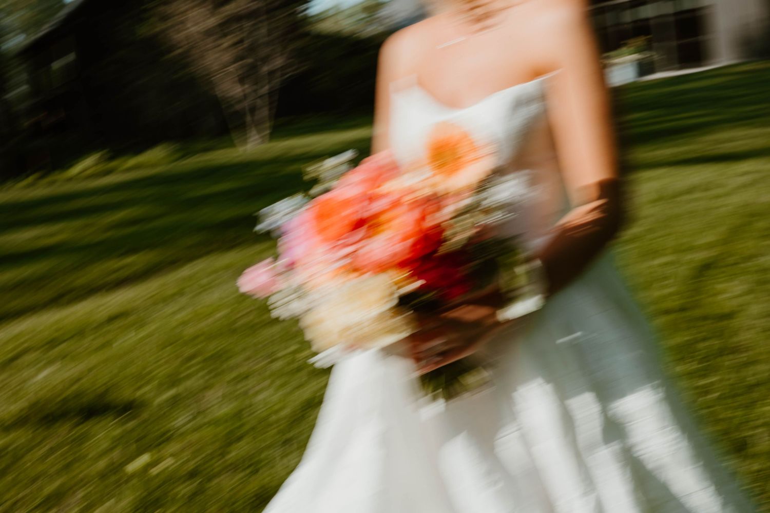Blurred motion shot of a bride in white gown holding a vibrant pink and orange wedding bouquet outdoors.
