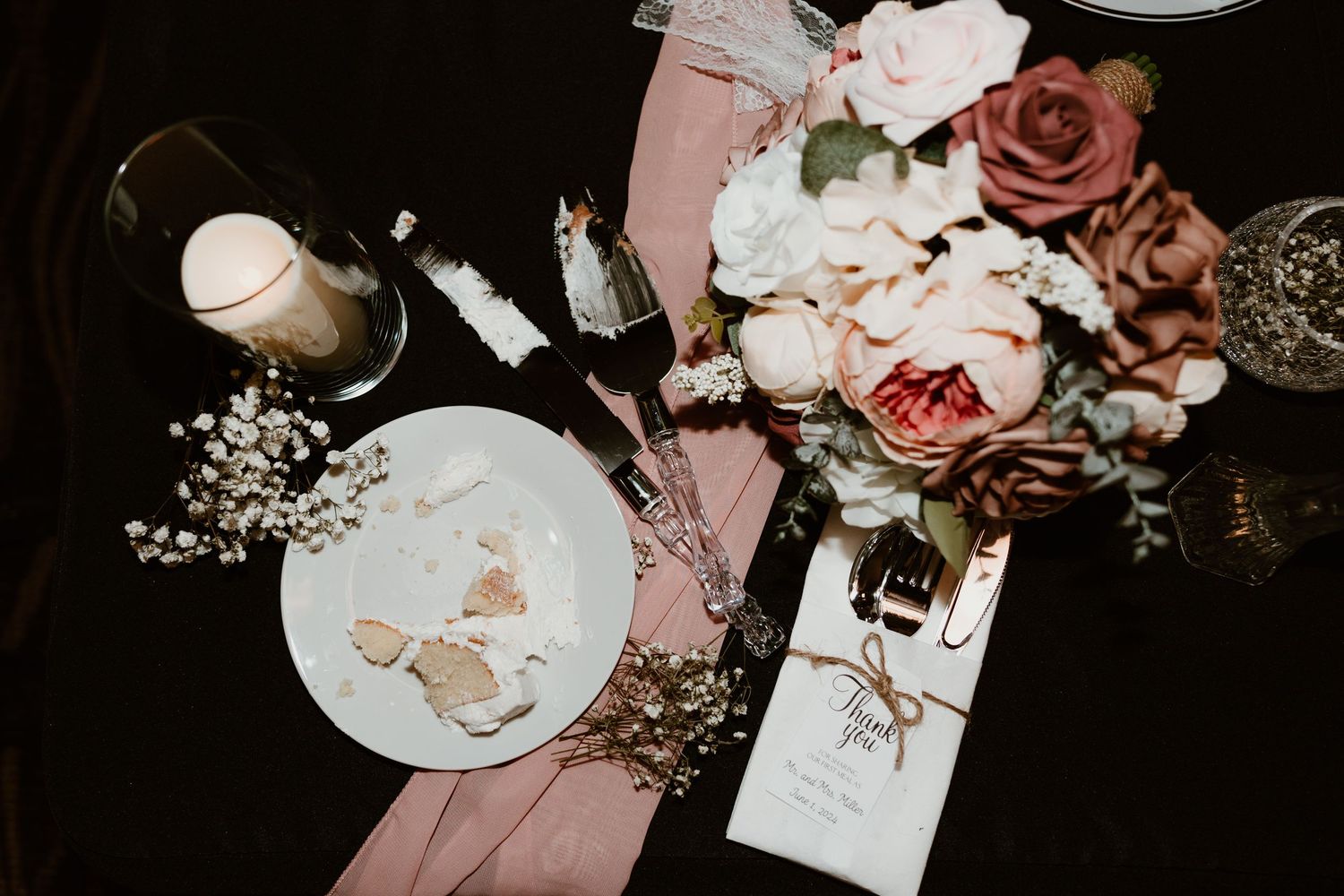 Wedding reception details with pink roses and candles arranged on a dark table.