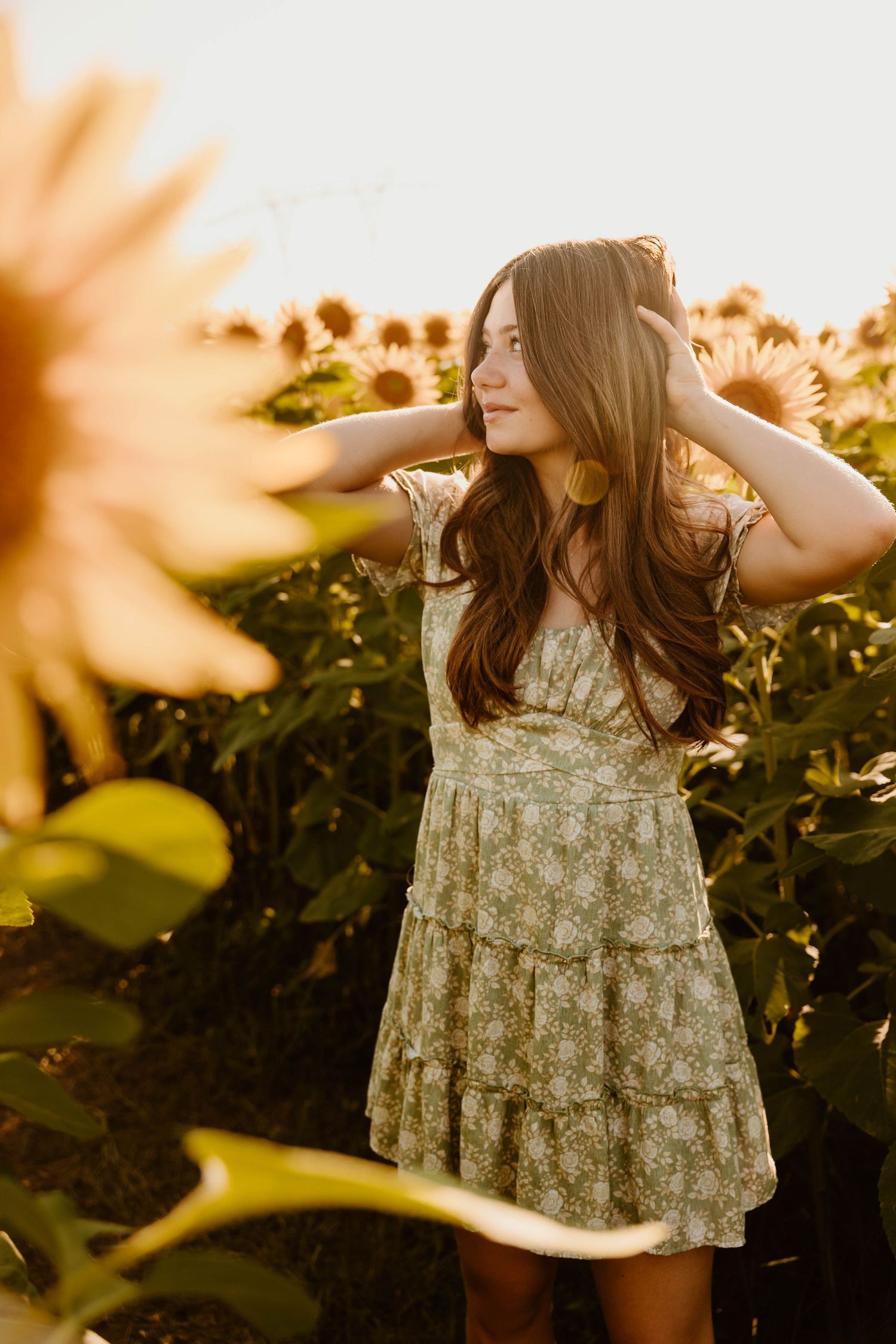 Woman in floral dress twirling in sunflower field at sunset.