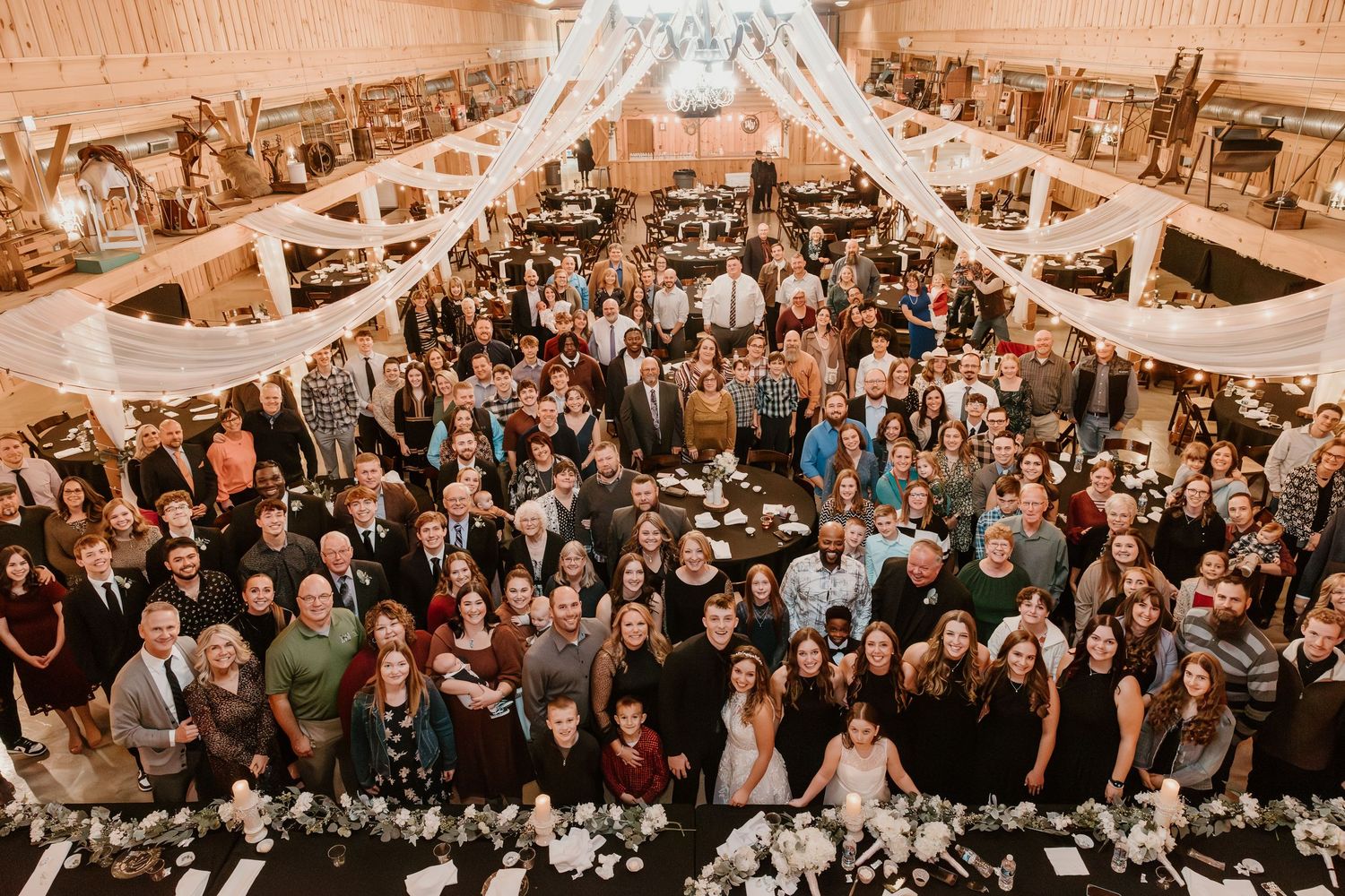 Large crowd gathered in an elegant reception venue with chandeliers and warm lighting.