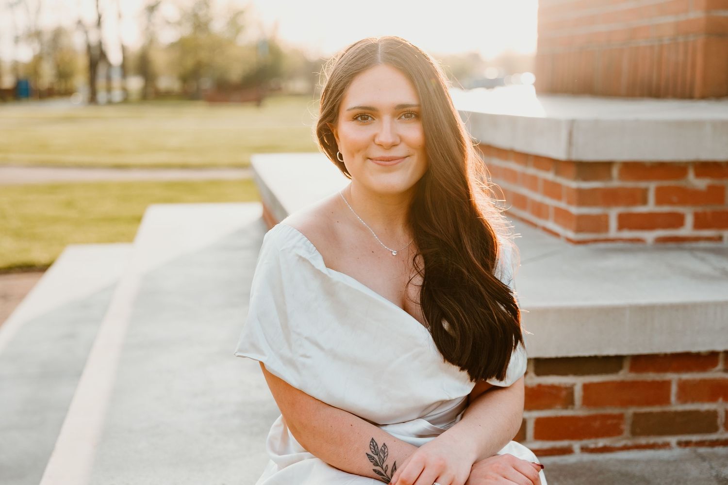 Person in graduation attire sitting on brick steps during golden hour.