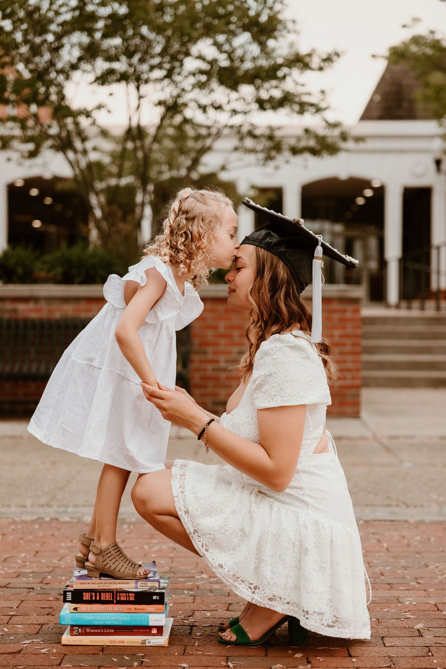 Person in white dress sits on brick ground reading books.